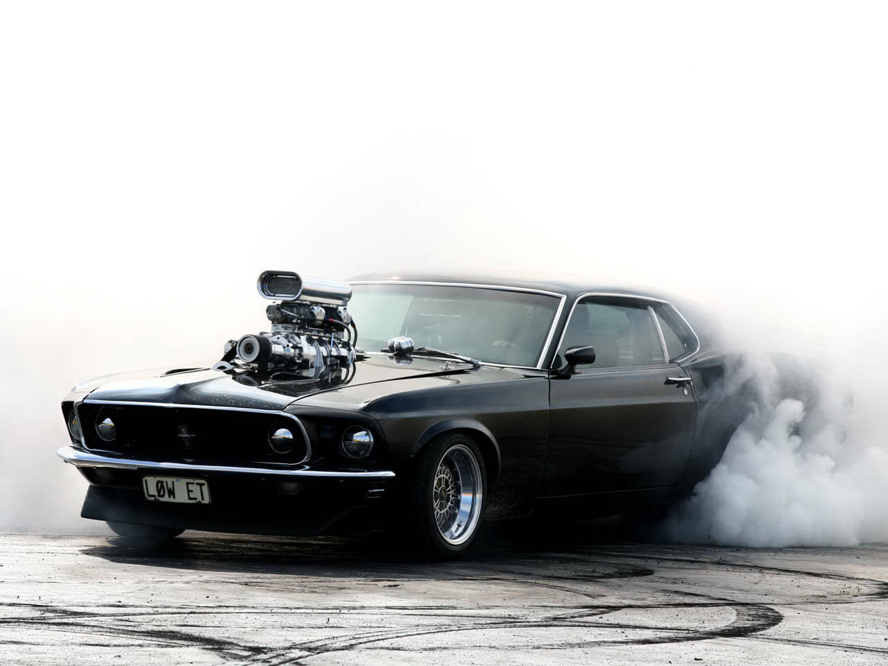 mustang HD 桌布 壁紙 — 一輛黑色經典肌肉車配備增壓引擎，在鋪設的賽道上燒胎，煙霧瀰漫。