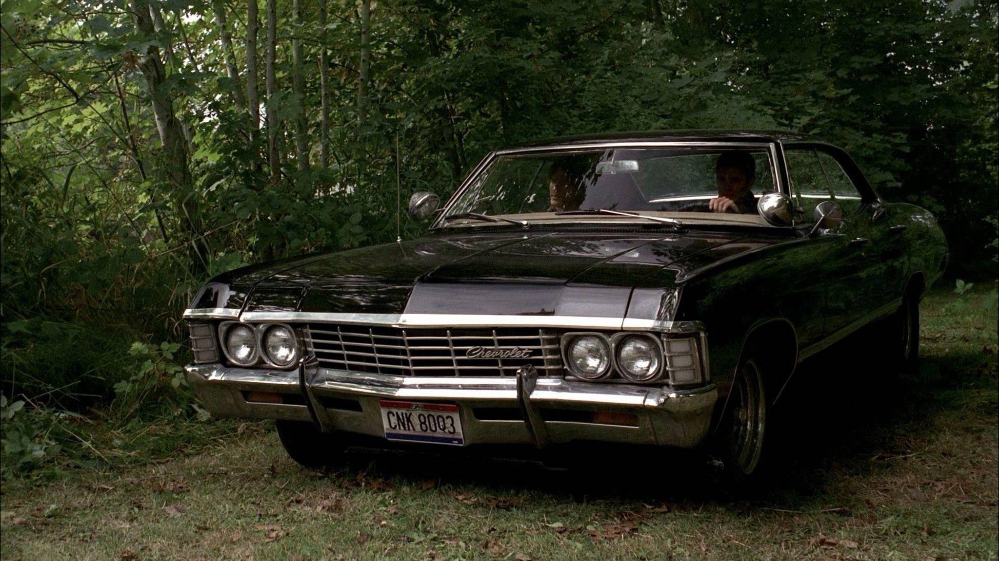 chevrolet impala 1967 桌布 壁紙 — 一輛黑色經典雪佛蘭敞篷車停放在茂密的綠色森林中，車內有兩個人。