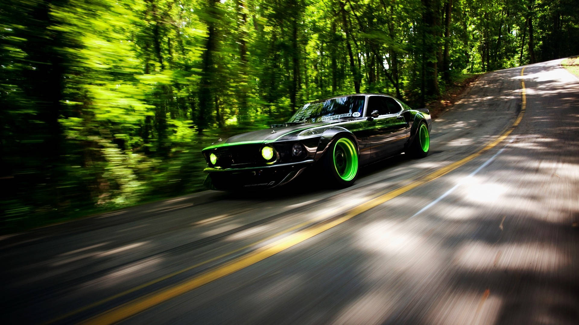 mustang HD 桌布 壁紙 — 一輛黑色肌肉車，帶有發光的綠色車輪，在陽光斑駁的林間道路上疾馳，帶有動態模糊效果。