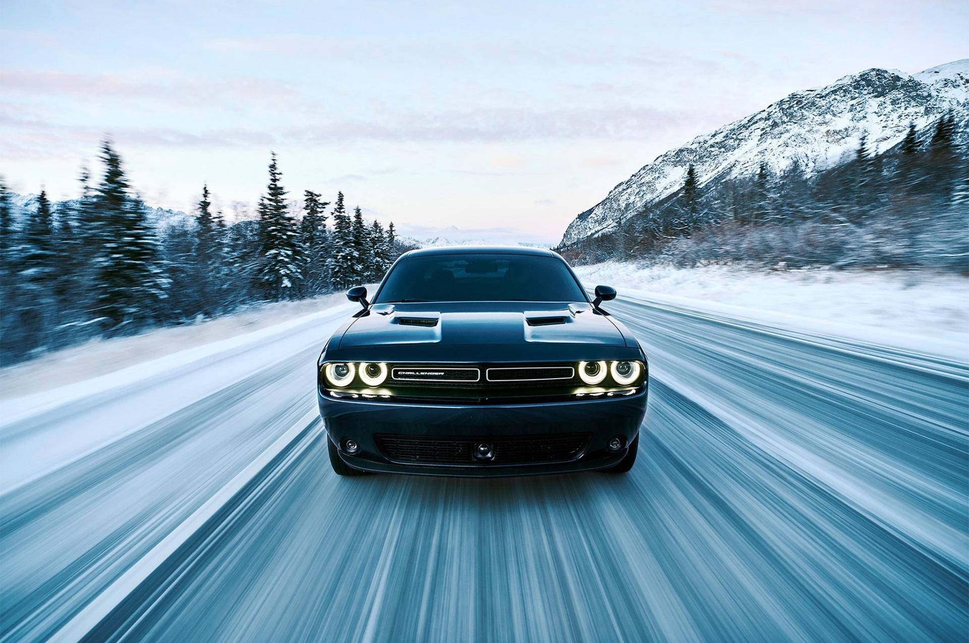 Challenger 桌布 壁紙 — 一輛黑色肌肉車在雪覆蓋的山路上疾馳，背景有動態模糊和松樹。
