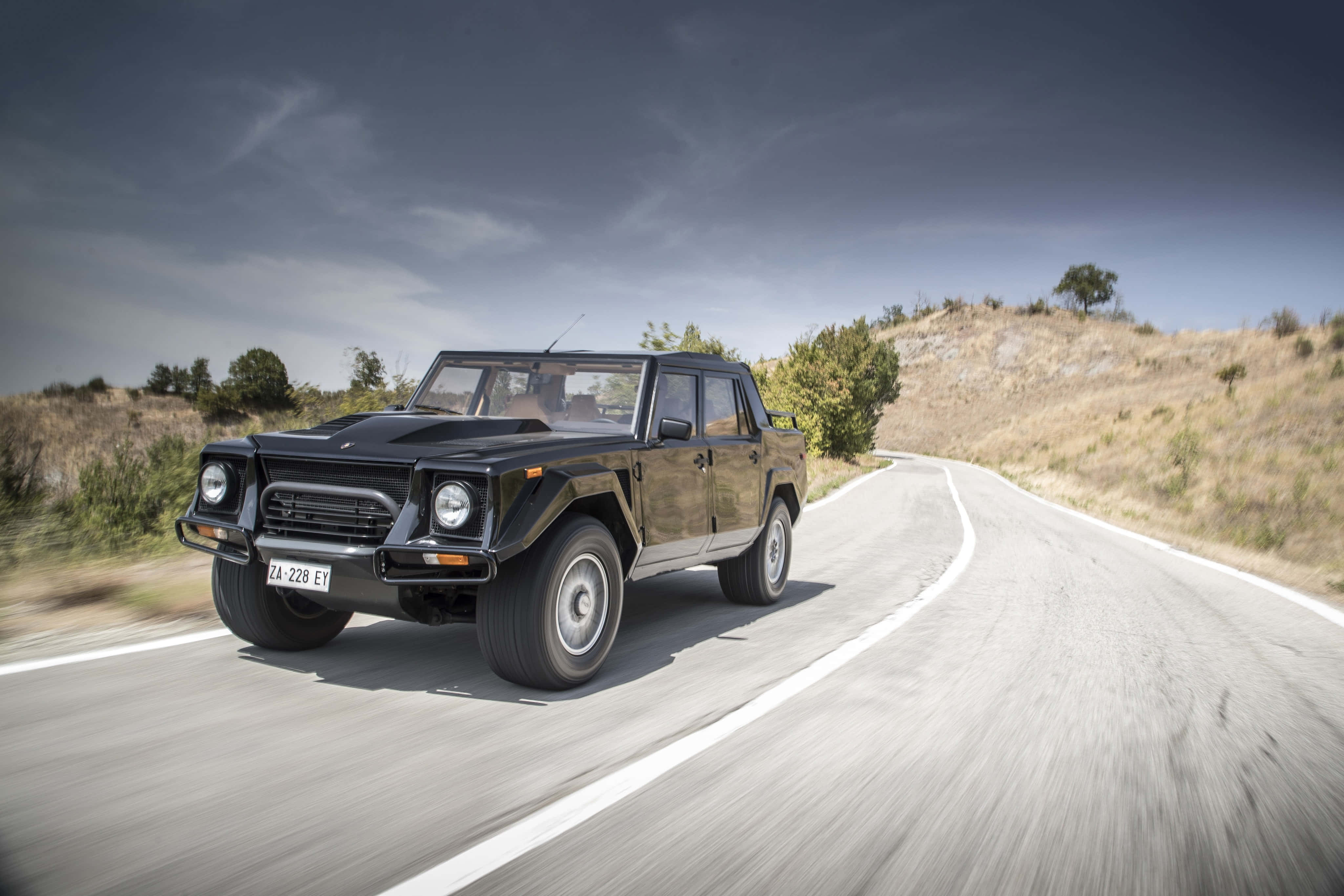 Lamborghini Lm002 桌布 壁紙 — 一輛黑色藍寶堅尼LM002 SUV在陰天下沿著蜿蜒的鄉村道路飛馳。