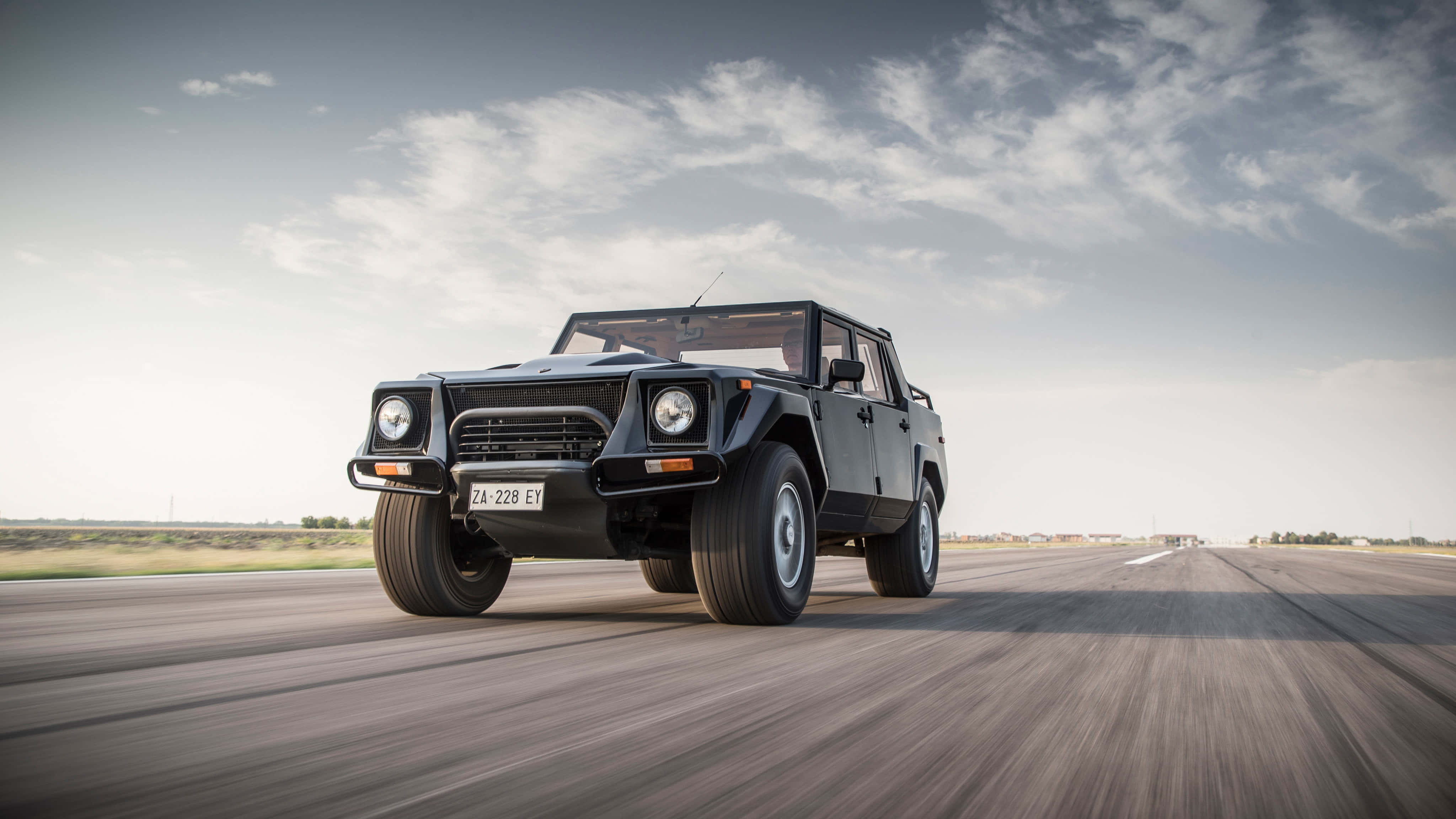 Lamborghini Lm002 桌布 壁紙 — 一輛黑色藍寶堅尼LM002 SUV在陰天下一條長直路上高速行駛，帶有模糊動態效果。