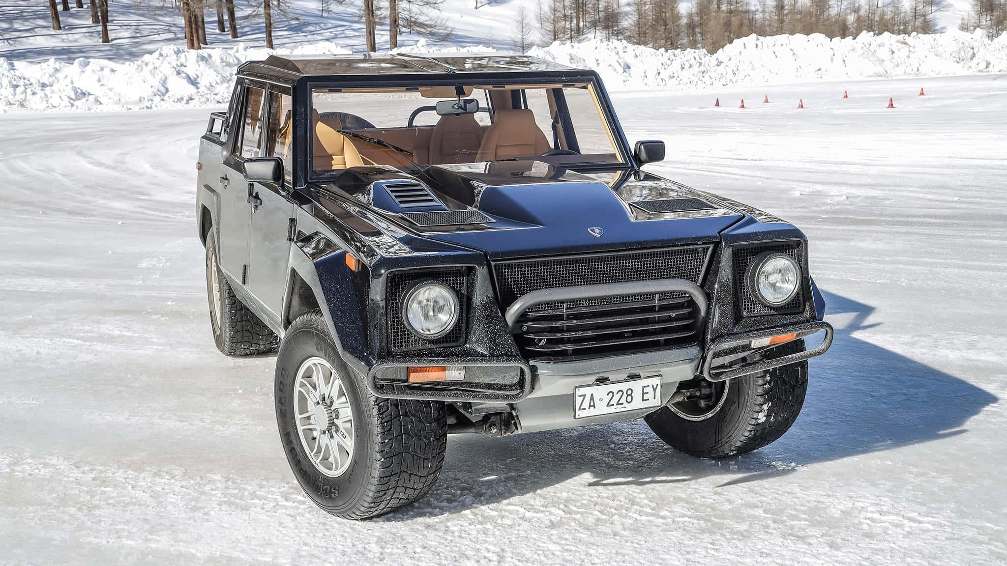 Lamborghini Lm002 桌布 壁紙 — 一輛黑色藍寶堅尼LM002 SUV（米色內裝）在明亮的日光下，佇立於以橙色三角錐標記的雪地賽道上。