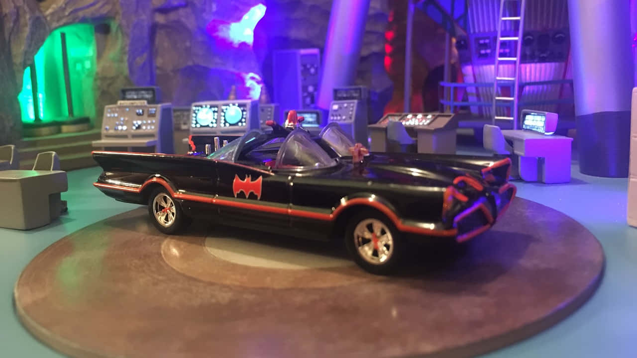 Batcave 桌布 壁紙 — 一輛黑色蝙蝠車帶有紅色蝙蝠標誌，放置在霓虹燈照亮的蝙蝠洞控制室的轉盤上。