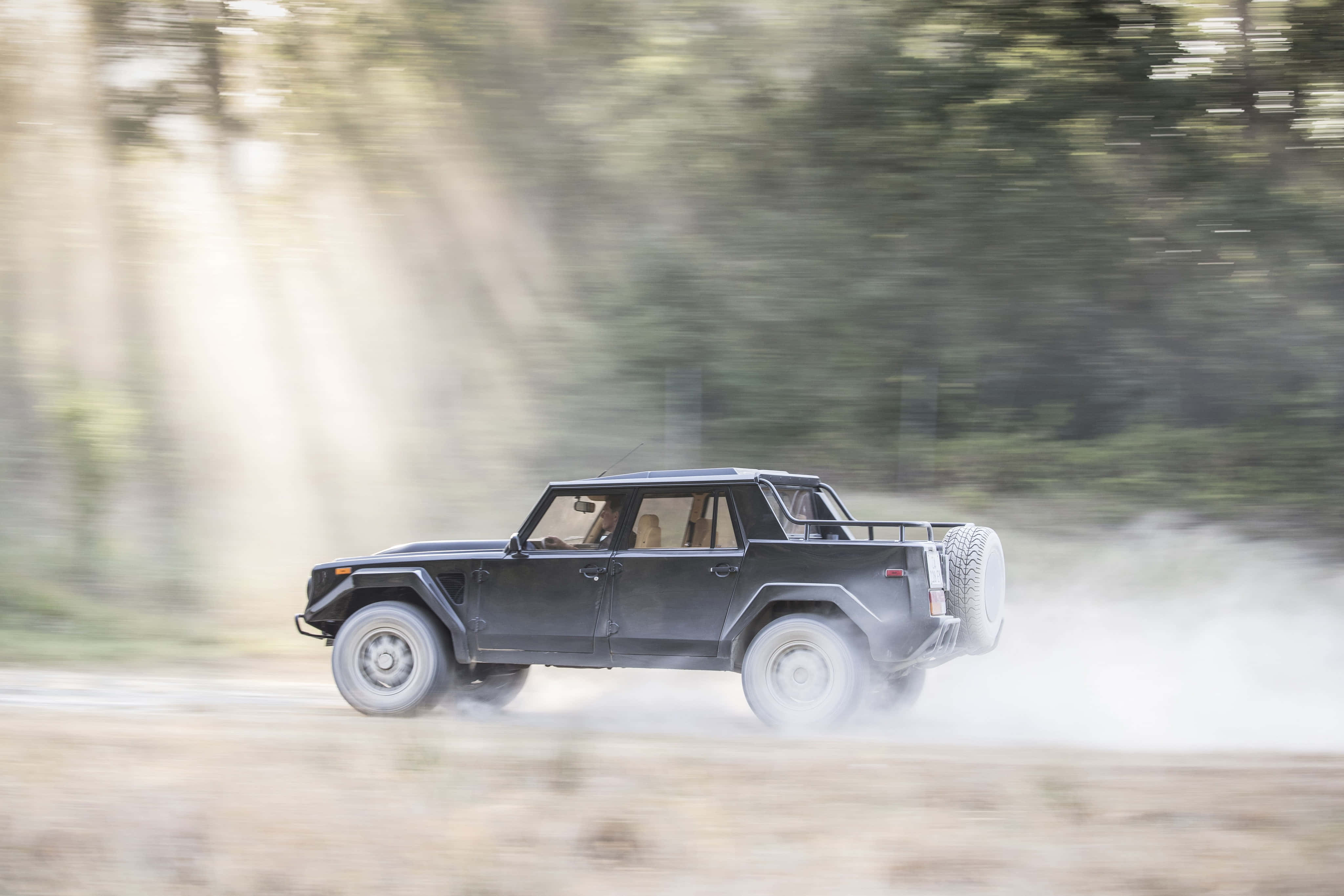 Lamborghini Lm002 桌布 壁紙 — 一輛黑色裝甲SUV在塵土飛揚的森林小徑上疾馳，揚起霧氣和動態模糊。