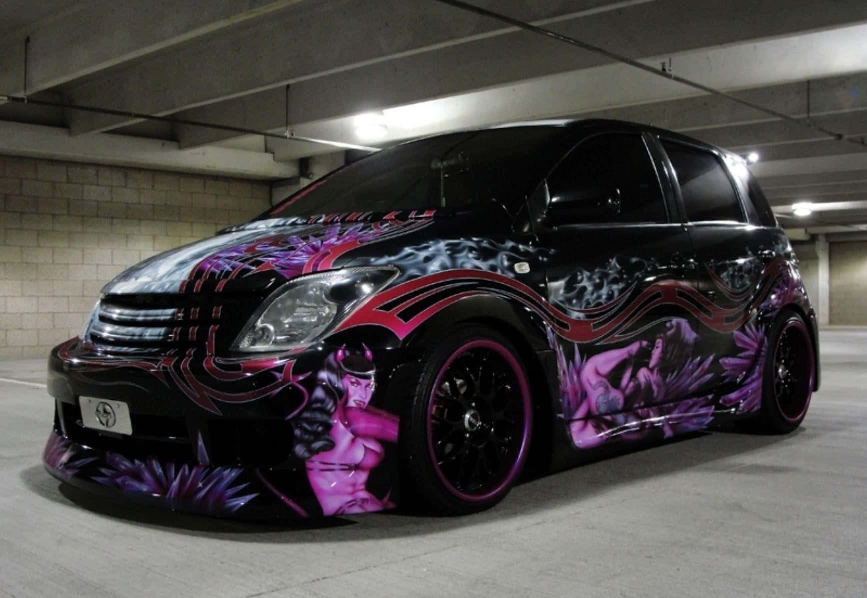Modified Car 桌布 壁紙 — 一輛黑色訂製汽車，帶有充滿活力的紫色和粉紅色惡魔主題塗鴉藝術，停在混凝土地下車庫中。