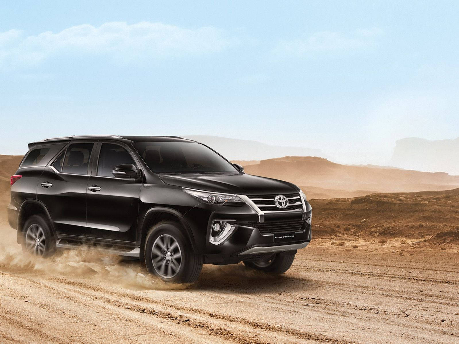 黑色 桌布 壁紙 — 一輛黑色豐田 Fortuner SUV 在晴朗的藍天下，穿越崎嶇的沙漠景觀，揚起塵土。