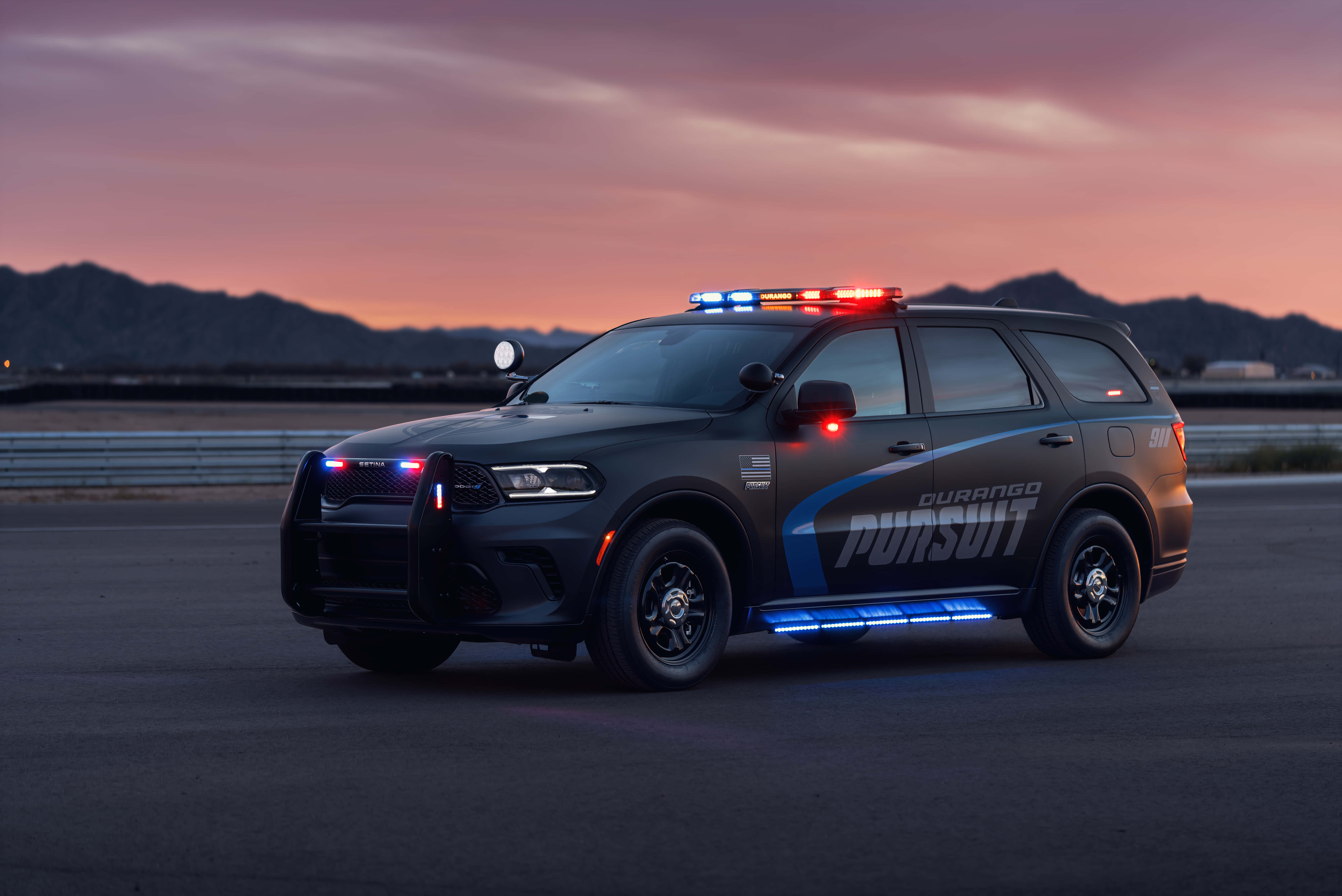 Law Enforcement 桌布 壁紙 — 一輛黑色道奇Durango Pursuit警用SUV，閃著警燈，停泊在黃昏時分空無一人的高速公路上，背景是山脈。
