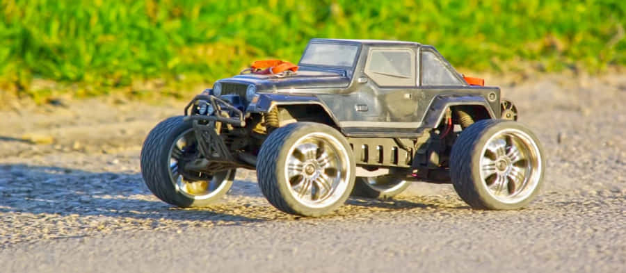 Rc Cars 桌布 壁紙 — 一輛黑色遙控怪獸卡車搭配銀色輪圈，停在碎石路旁，旁邊有綠草。