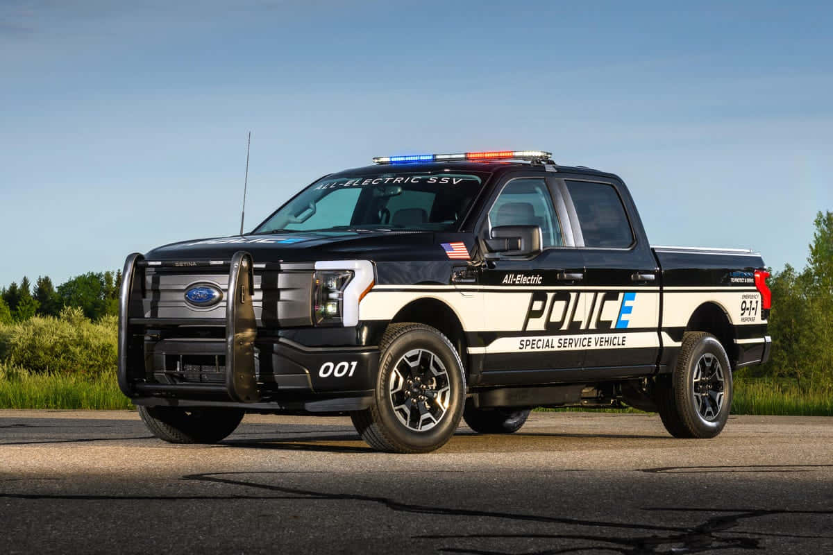 Police Car 桌布 壁紙 — 一輛黑色電動警車閃著燈停在柏油路上，天空湛藍。