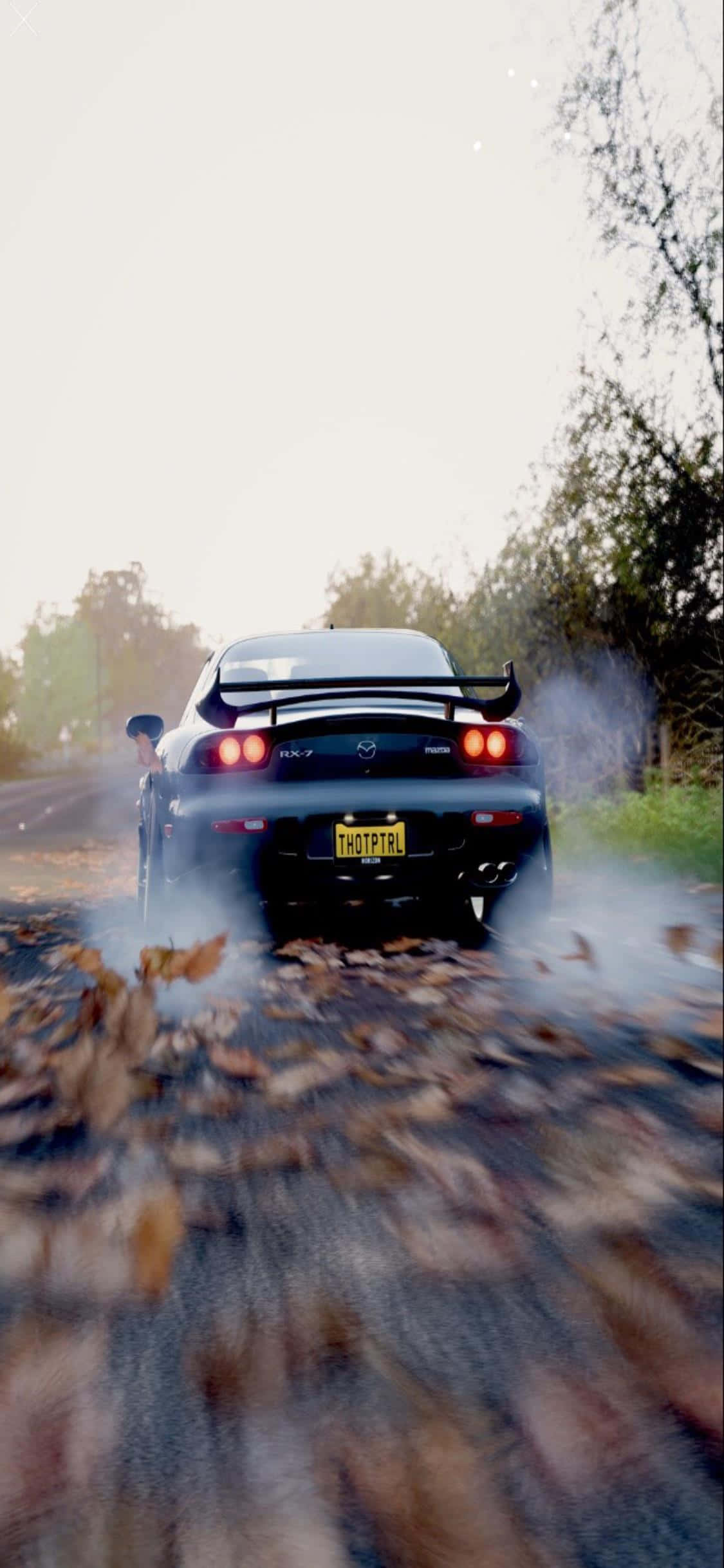 iPhone Xs Forza Horizon 4 桌布 壁紙 — 一輛黑色馬自達RX-7在黃金時段的鄉村道路上穿過秋葉飄移。