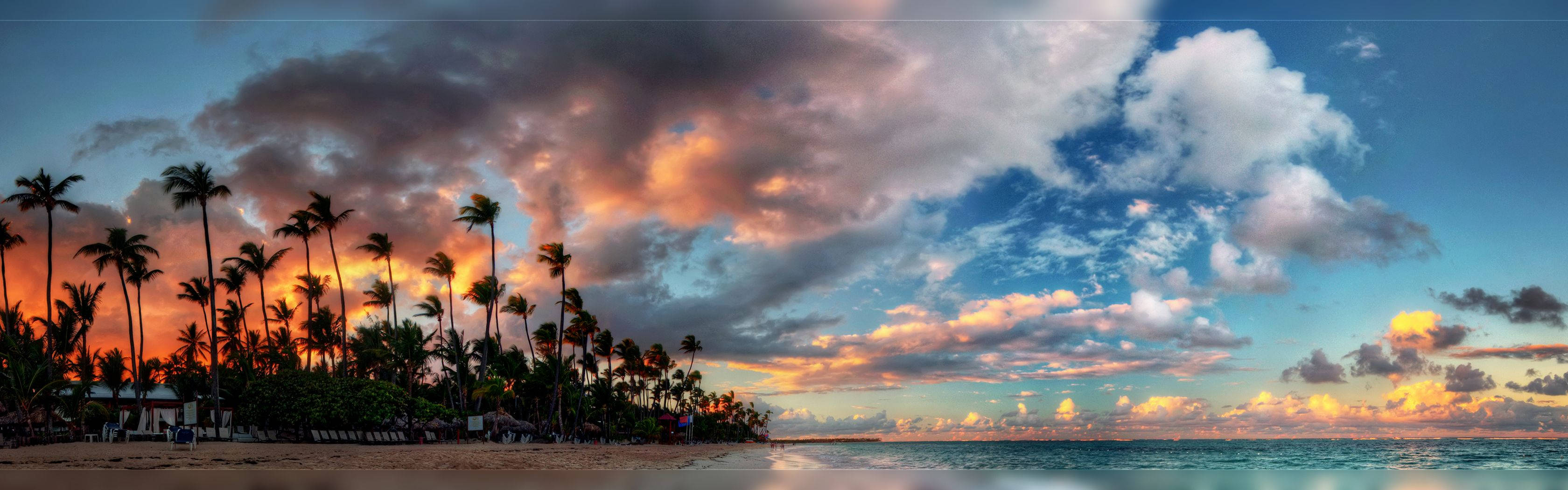 Screen 桌布 壁紙 — 一輪充滿活力的夕陽將天空染成火熱的橙色和粉紅色，照耀在棕櫚樹成蔭的熱帶海灘上。