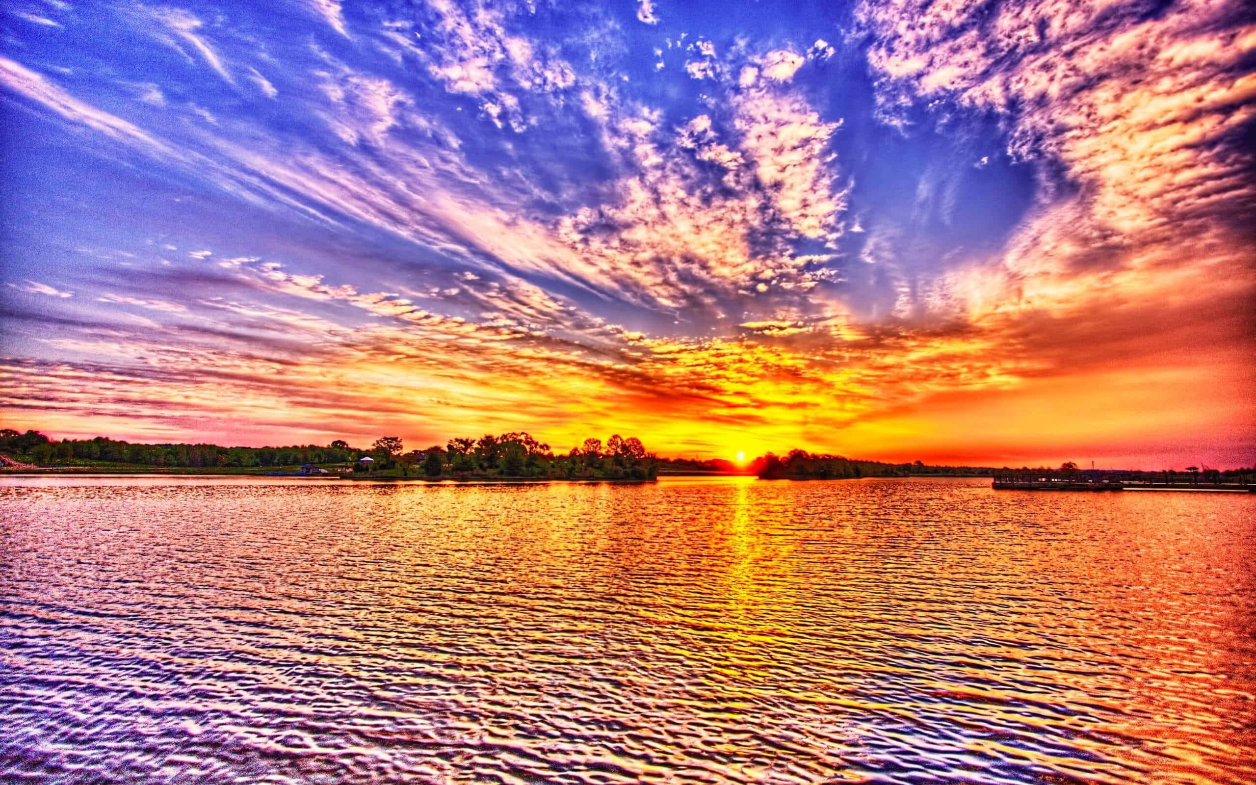 Beautiful Sky 桌布 壁紙 — 一輪充滿活力的夕陽將天空染成火熱的橙色和紫色，映照在平靜的湖面上，反射出閃爍的地平線。