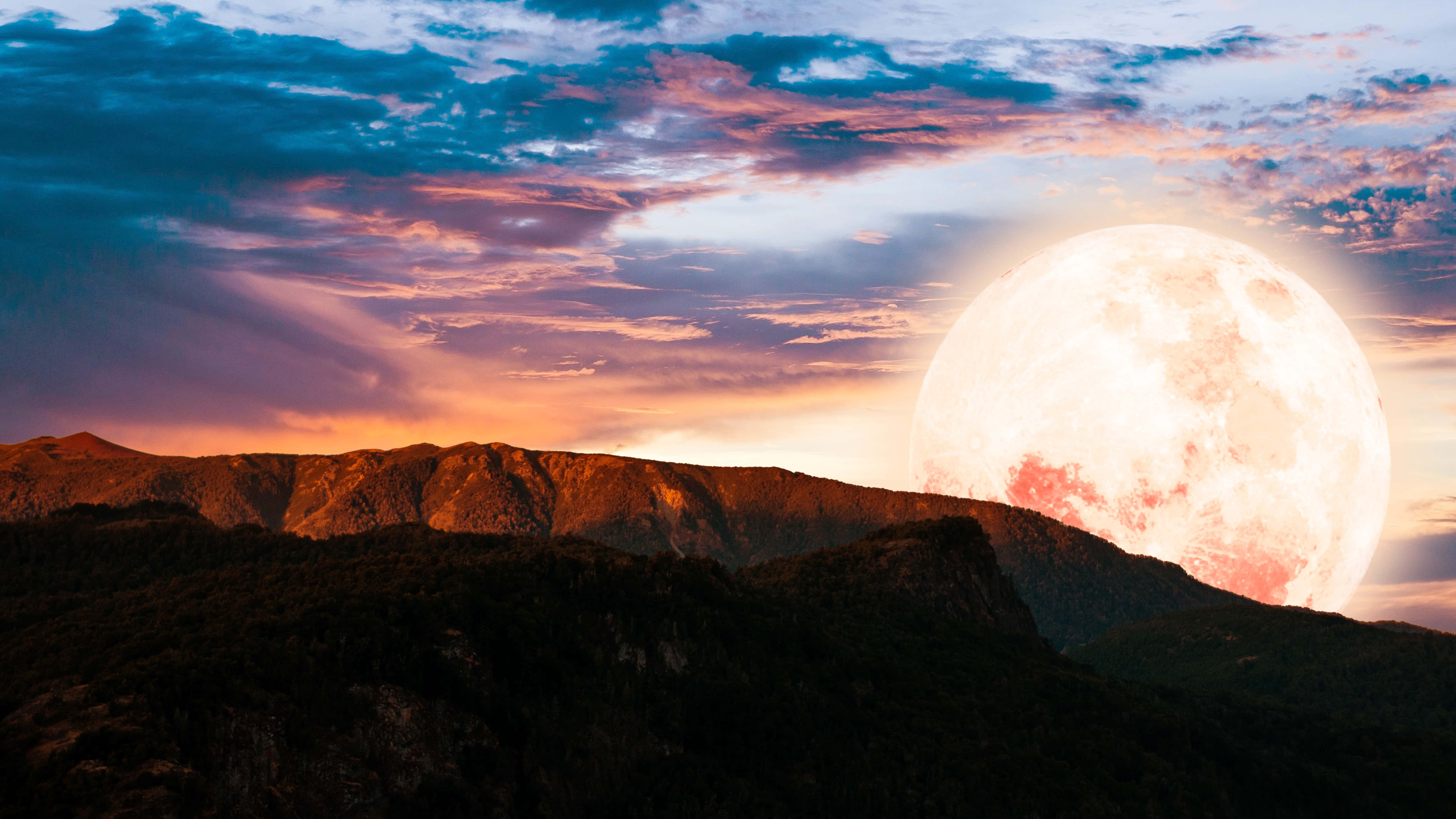 Moon Aesthetic 桌布 壁紙 — 一輪巨大的發光月亮在崎嶇的山峰後升起，天空充滿活力，佈滿粉紅、橙色和深藍色的雲彩。