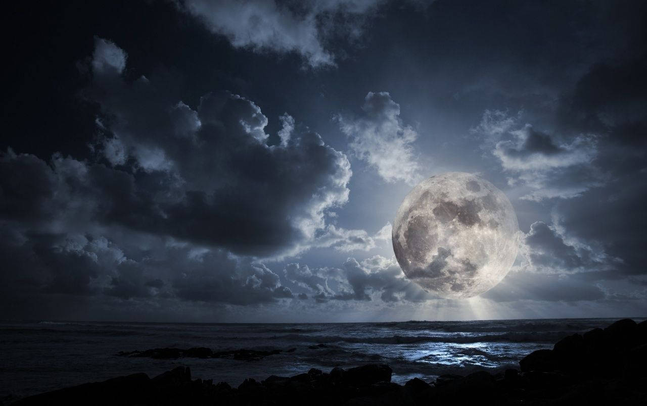 黑夜 桌布 壁紙 — 一輪巨大的發光月亮穿透戲劇性的暴風雲，照耀在岩石海岸的黑暗海洋上。