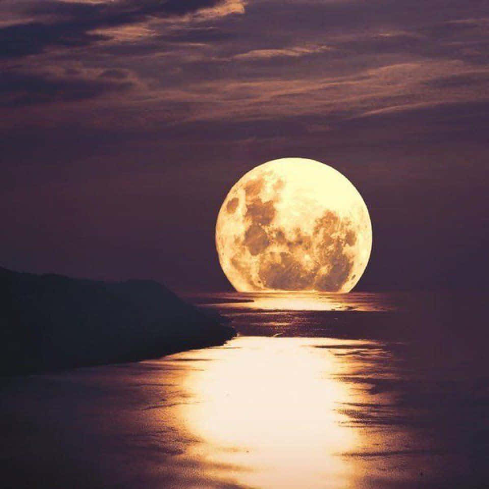 Beautiful Moon 桌布 壁紙 — 一輪巨大的發光滿月在平靜的海洋上升起，在深紫色的天空下，在水面上投下金色的倒影。