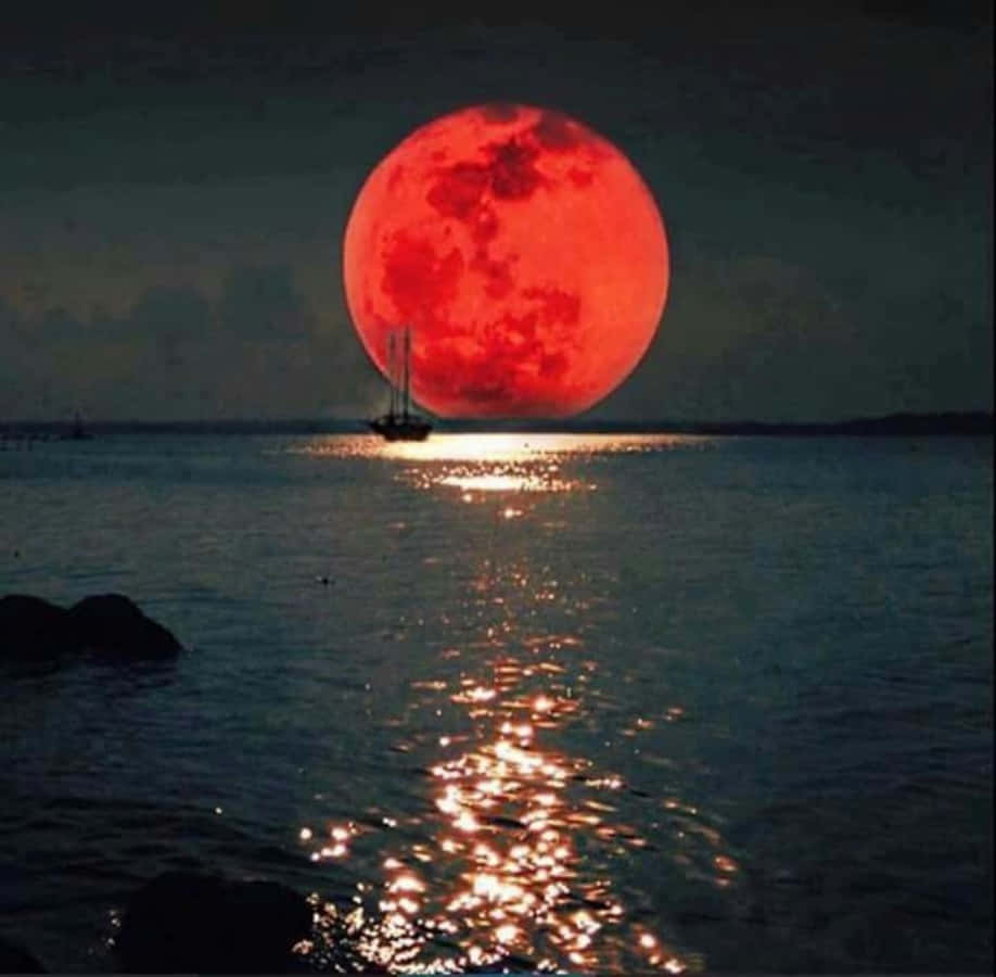 Beautiful Moon 桌布 壁紙 — 一輪巨大的血紅色月亮在平靜的海面上升起，一艘帆船在其光芒下呈現剪影。