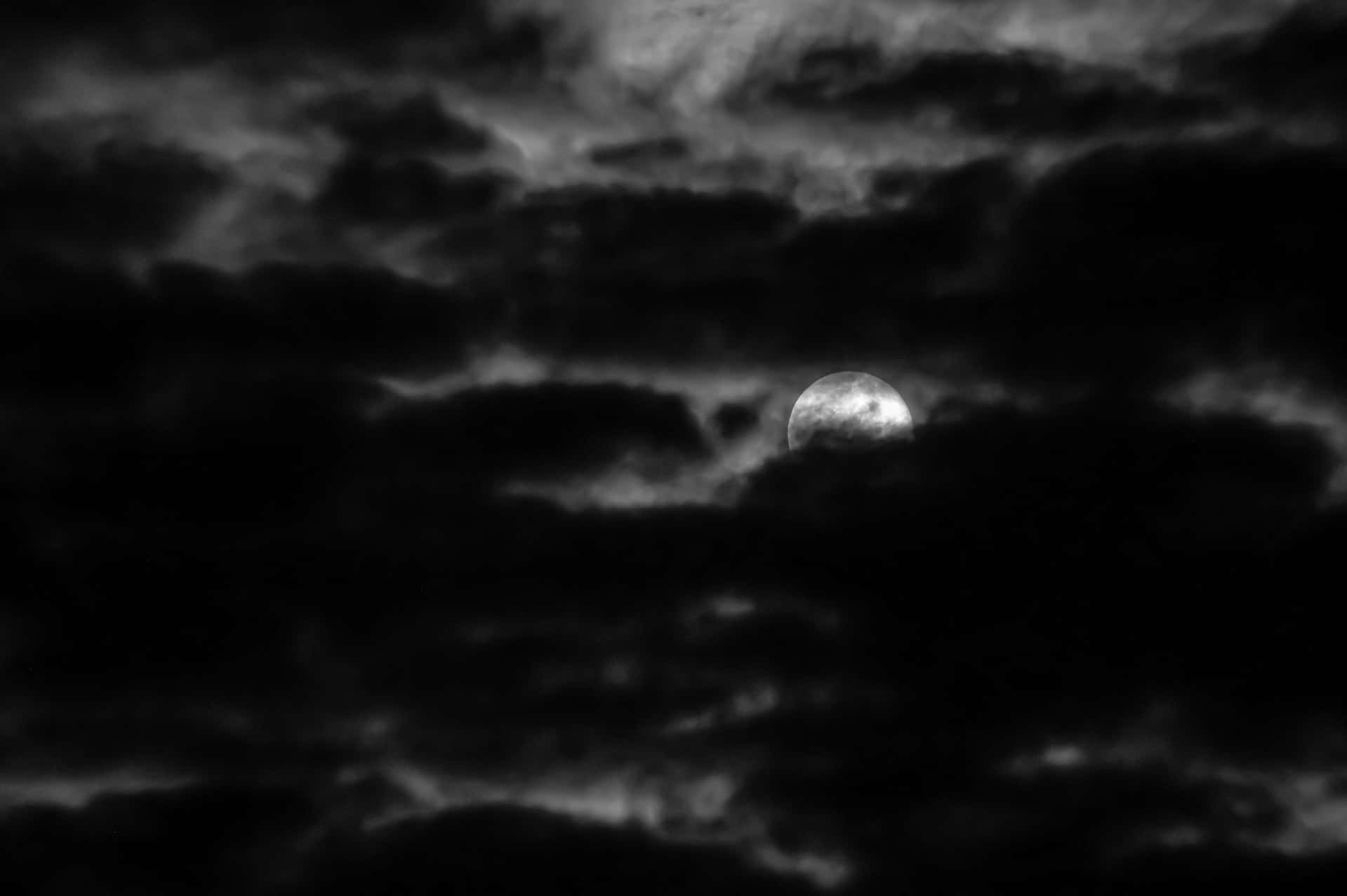 Dark Moon 桌布 壁紙 — 一輪明亮的月亮在濃密旋轉的雲層中窺視，映襯著 stark 的單色夜空。