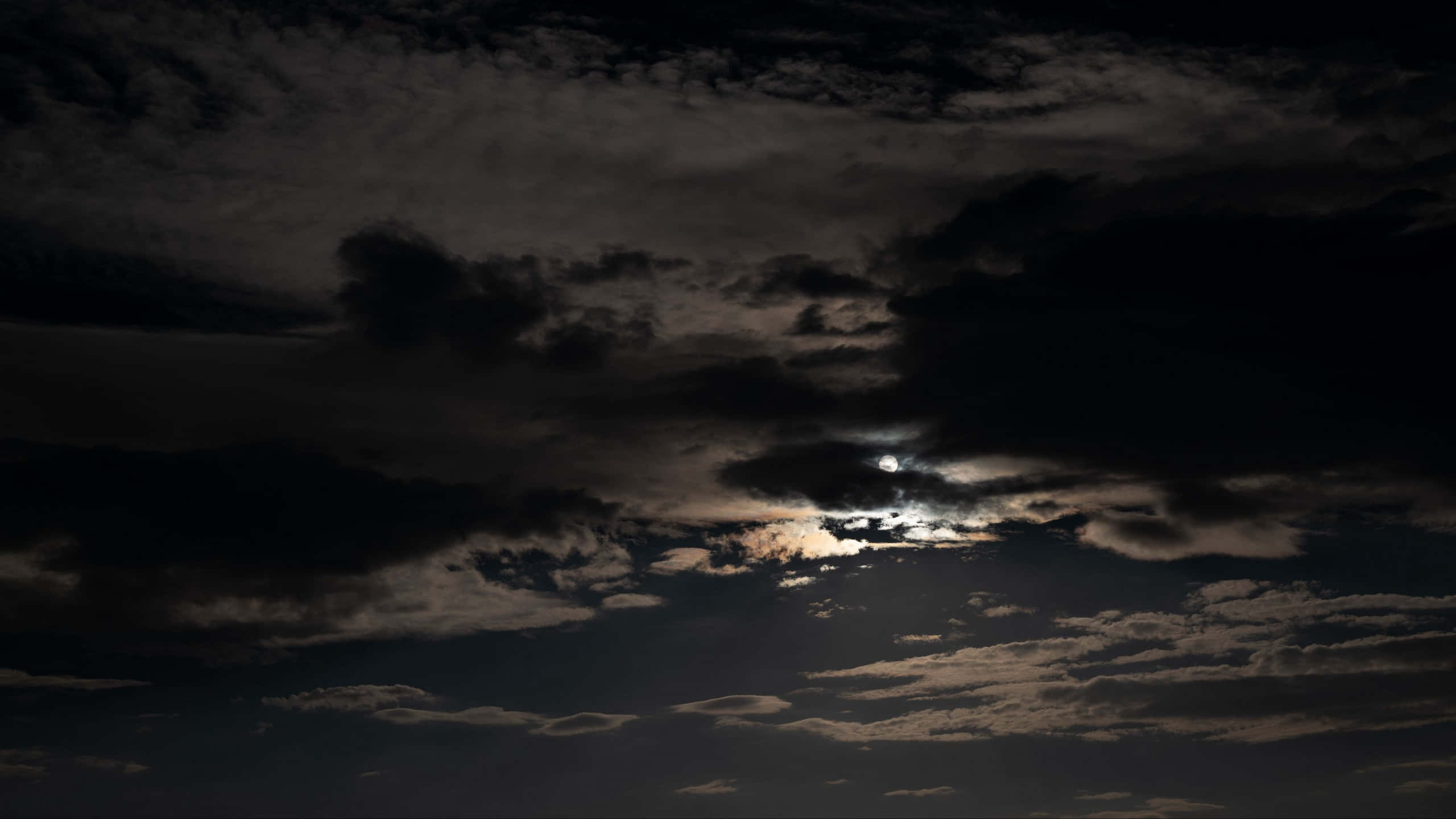 黑夜 桌布 壁紙 — 一輪明亮的月亮穿透濃密的烏雲，在陰鬱的夜空中灑下空靈的光芒。