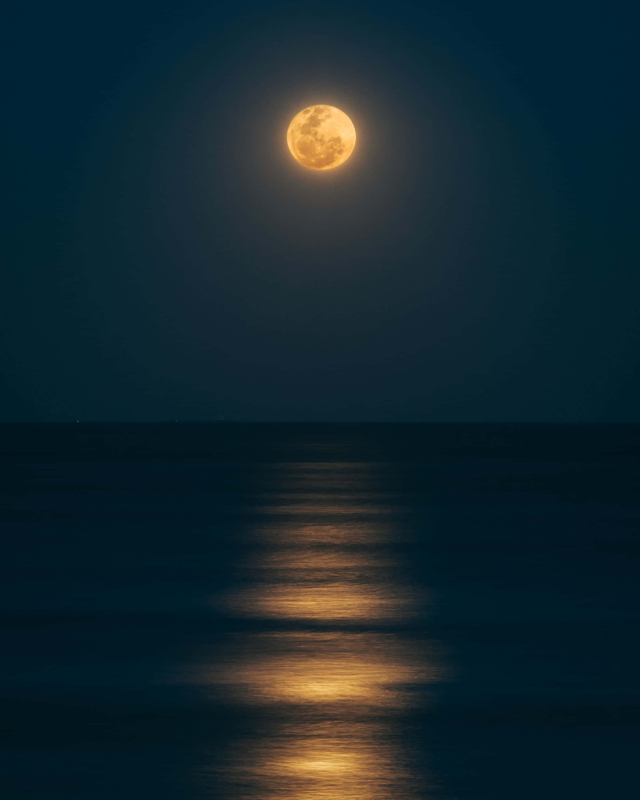 Dark Ocean 桌布 壁紙 — 一輪明亮的滿月在平靜的海洋上空發光，在黑暗的水面上投下一條金色的光路。