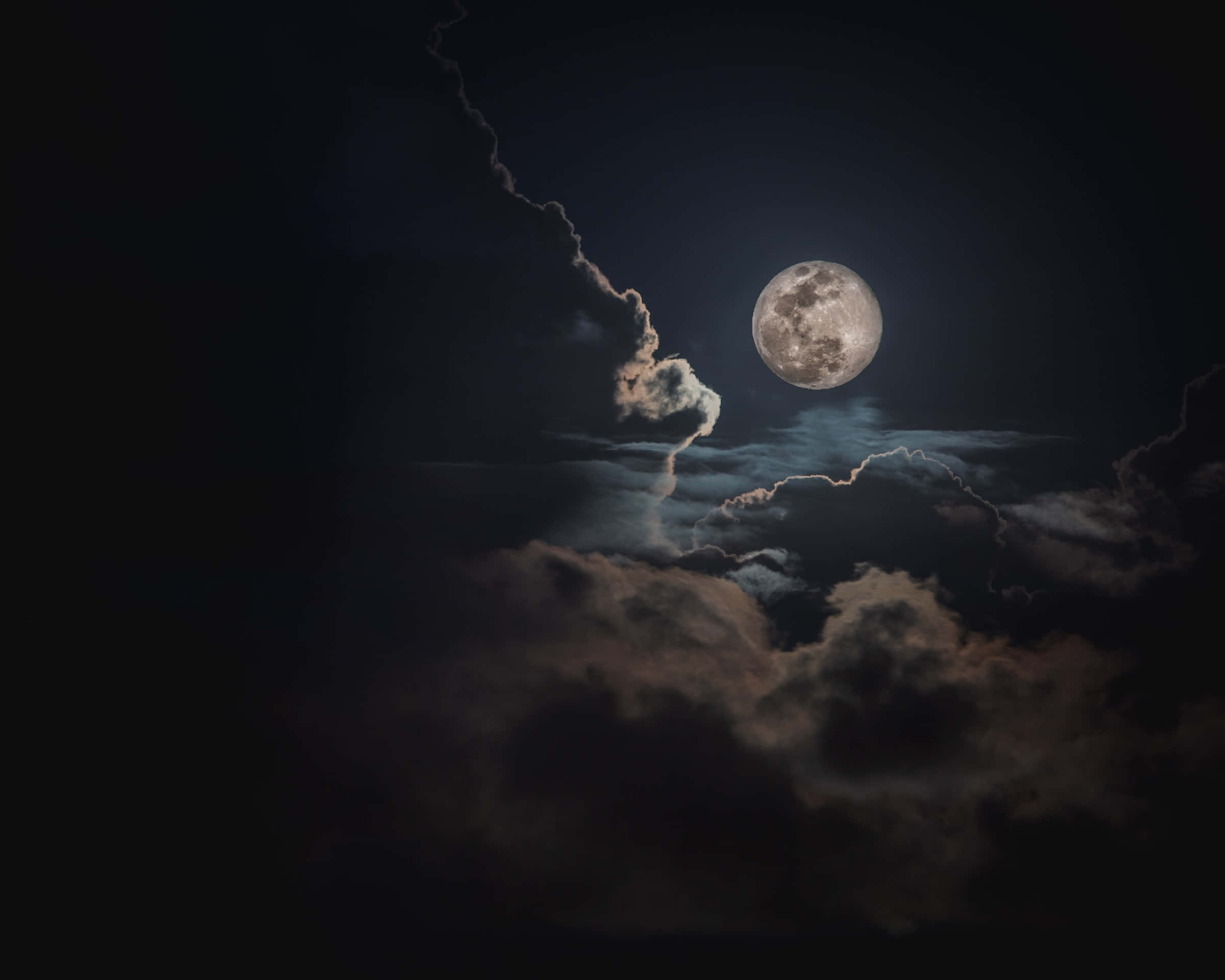 Dark Moon 桌布 壁紙 — 一輪明亮的滿月在戲劇性的烏雲中發光，映照在陰鬱的夜空。