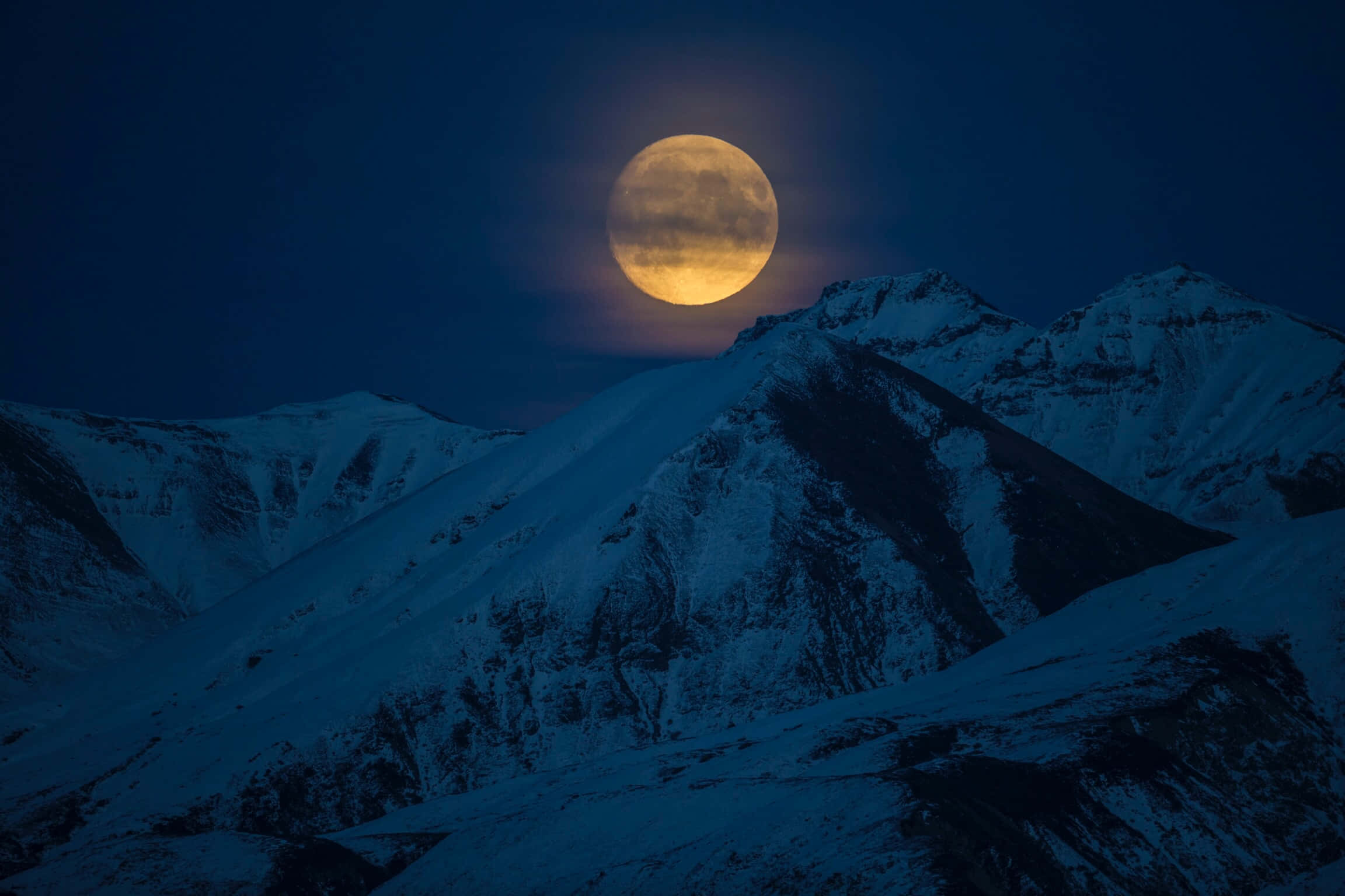 圖片 桌布 壁紙 — 一輪明亮的滿月在深藍色夜空下照耀著積雪的山峰。