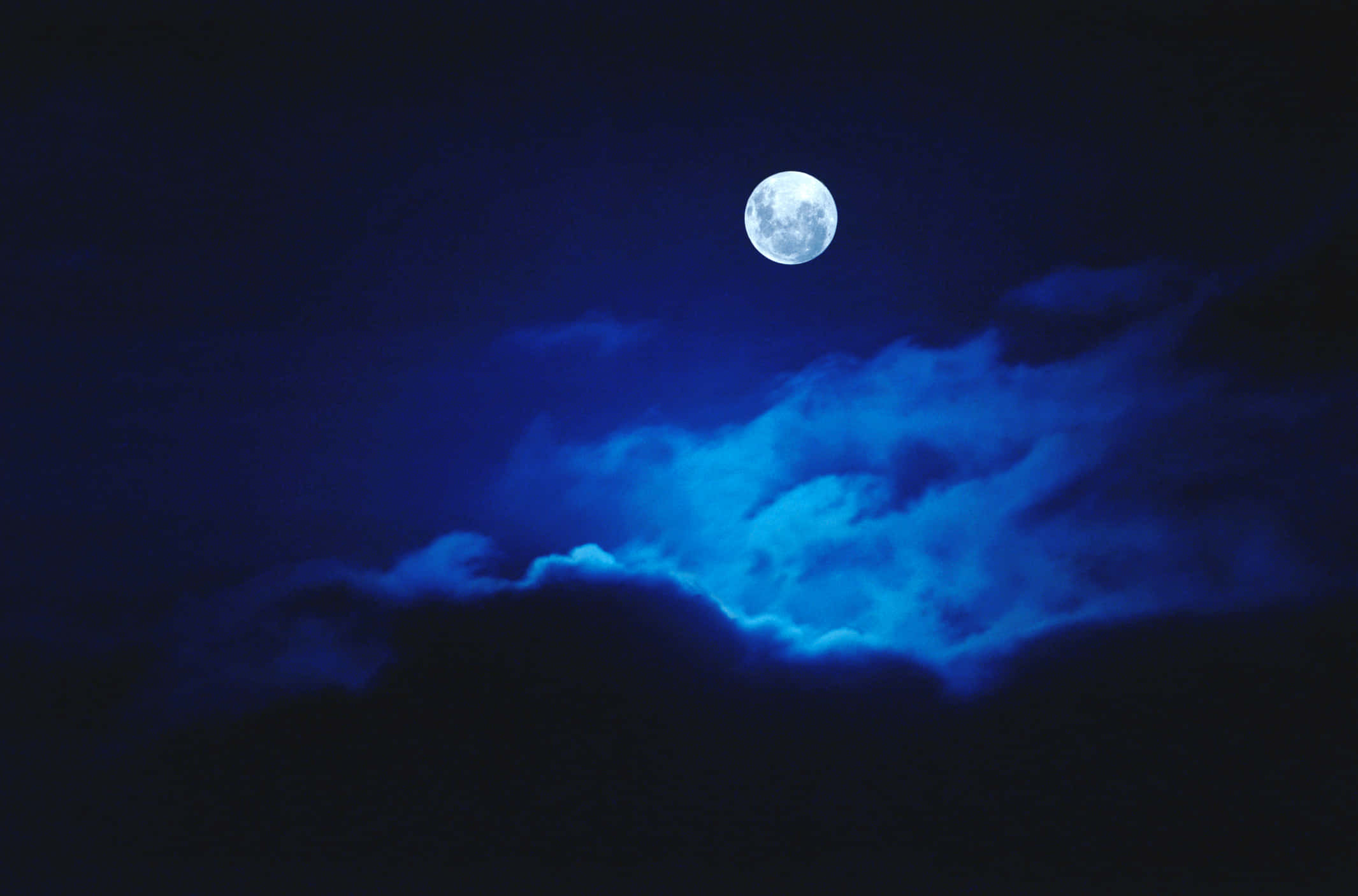 夜空 桌布 壁紙 — 一輪明亮的滿月在深藍色漩渦雲層上方發光，映照在深邃的夜空。