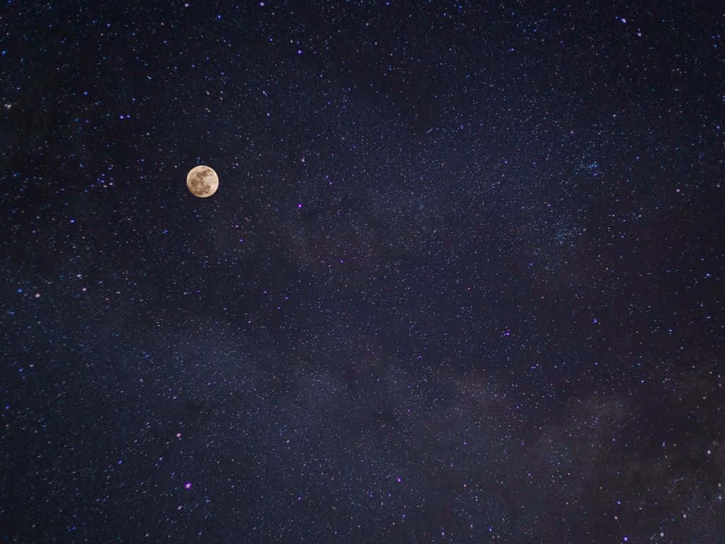 月亮與星星 桌布 壁紙 — 一輪明亮的滿月在深靛藍色夜空中，於密集的星星和宇宙塵埃之間閃耀。