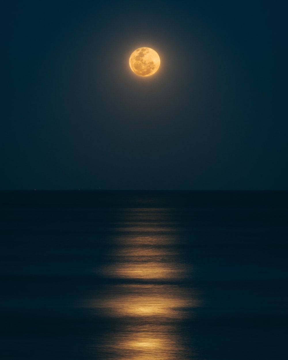 黑夜 桌布 壁紙 — 一輪明亮的滿月在深靛藍色的夜空下，在平靜的海洋上投射出一條金色的小徑。