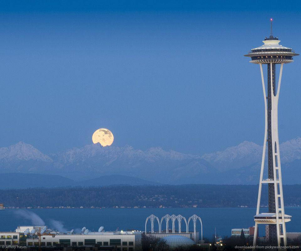 Space Needle 桌布 壁紙 — 一輪明亮的滿月在積雪的山峰後升起，太空針塔在深藍色的暮色天空中巍然聳立。