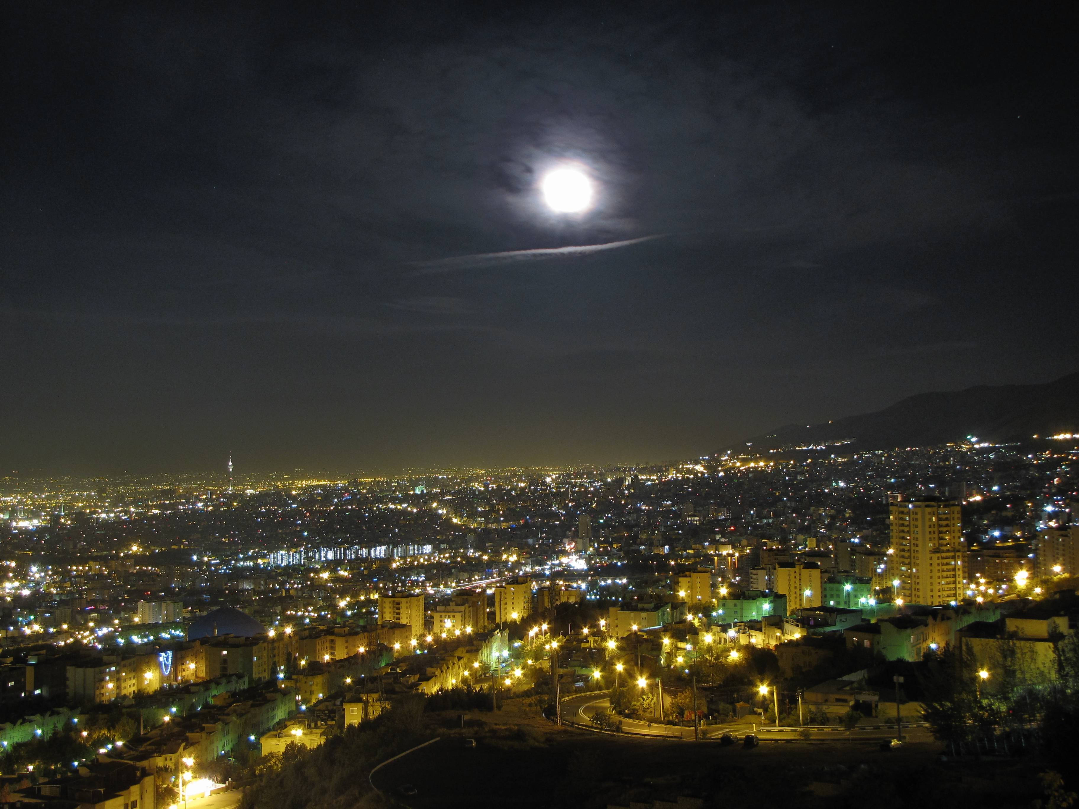 Tehran 桌布 壁紙 — 一輪明亮的滿月懸掛在夜晚廣闊的城市景觀上空，其光芒照亮了下方無數的路燈和建築物。