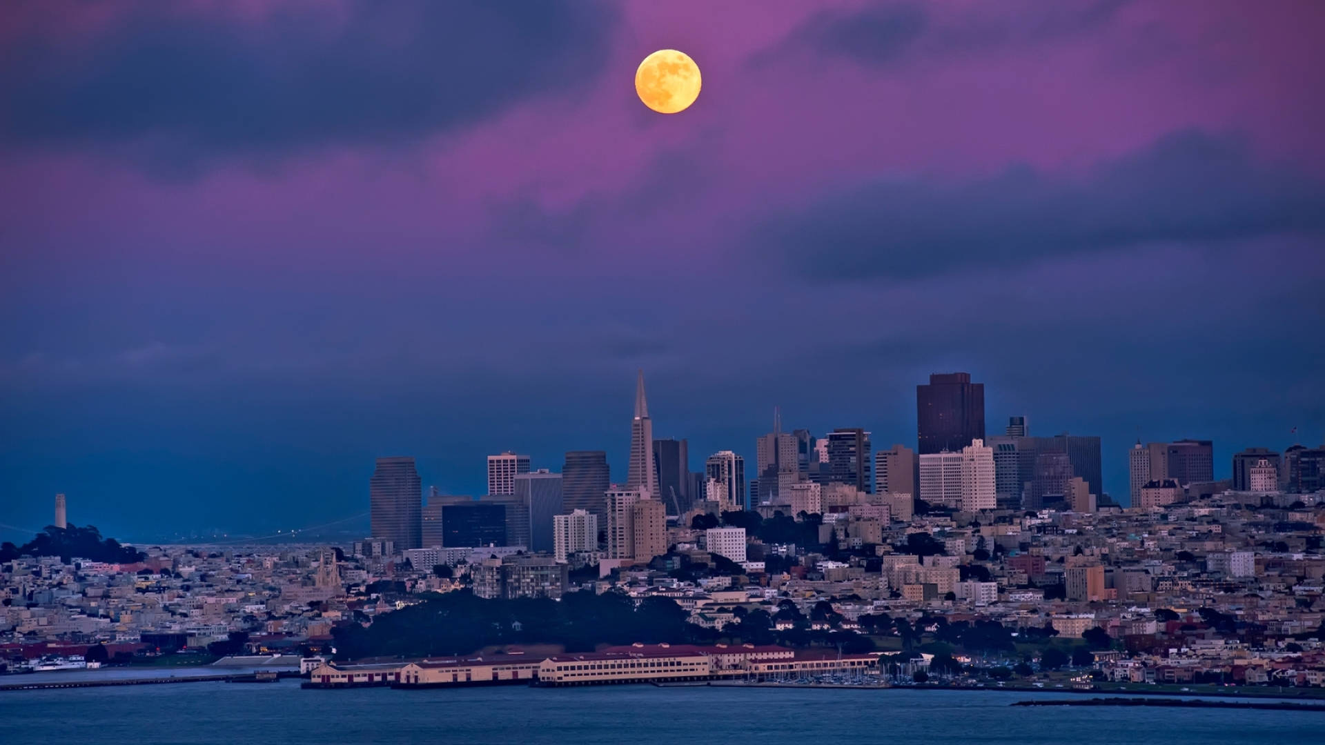 San Francisco HD 桌布 壁紙 — 一輪明亮的滿月懸掛在黃昏的舊金山天際線上，為城市景觀和海灣投下紫色和藍色的色調。