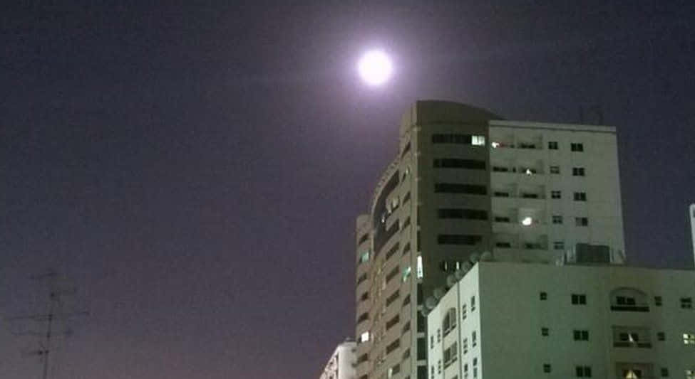 Perigee 桌布 壁紙 — 一輪明亮的滿月照耀著夜晚中一群現代公寓大樓，部分窗戶亮著燈。