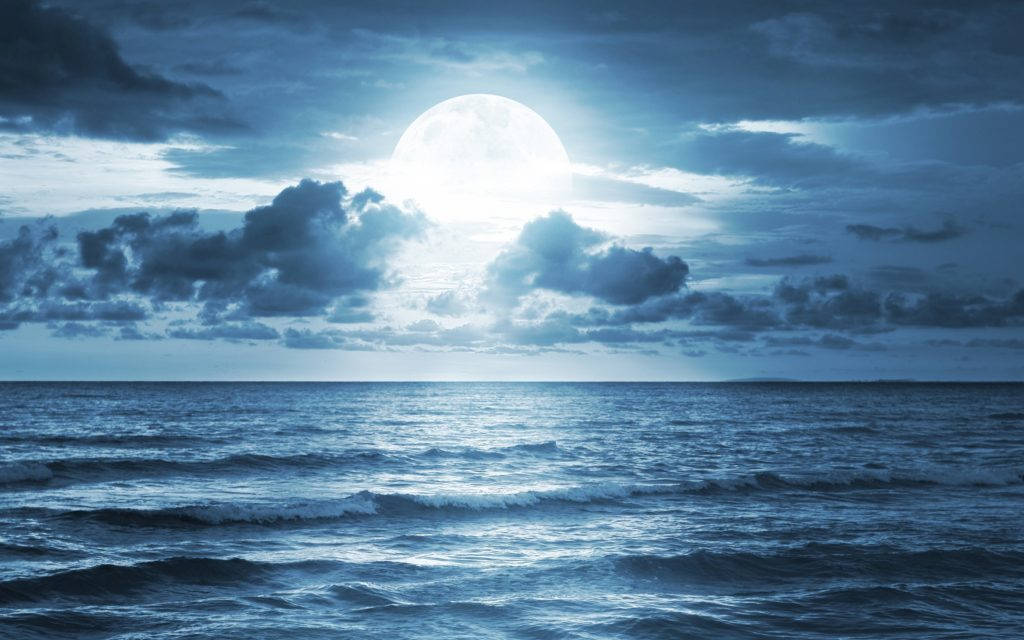 Moonlight 桌布 壁紙 — 一輪明亮的滿月穿透戲劇性的雲層，照耀在深藍夜空下廣闊起伏的海洋上。