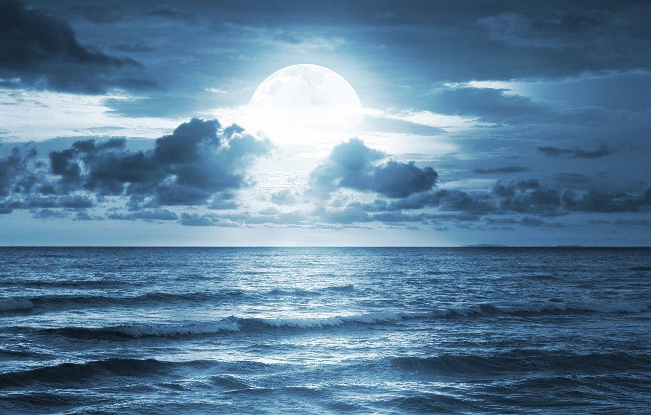 月夜星空 桌布 壁紙 — 一輪明亮的滿月穿透戲劇性的雲層，照耀在深藍色暮色天空下廣闊起伏的海洋之上。