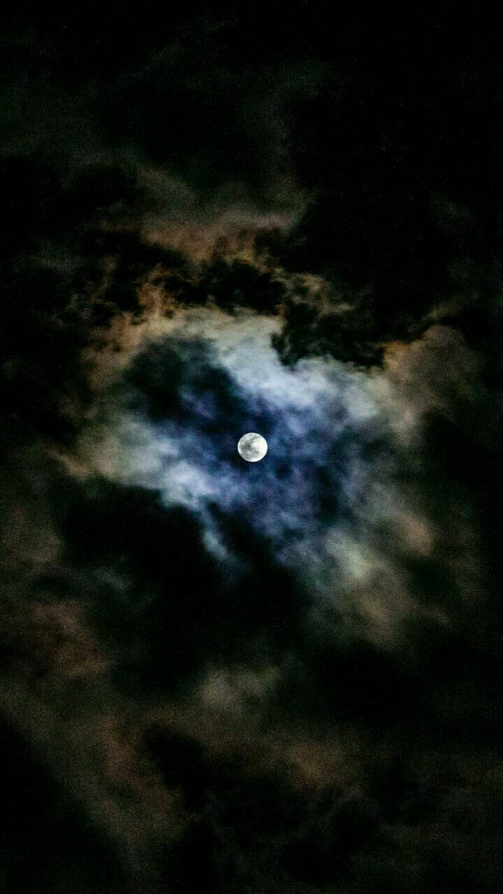 Moon Aesthetic 桌布 壁紙 — 一輪明亮的滿月穿透旋轉的暗雲，散發出空靈的藍色和橙色光芒，映襯著深邃的夜空。