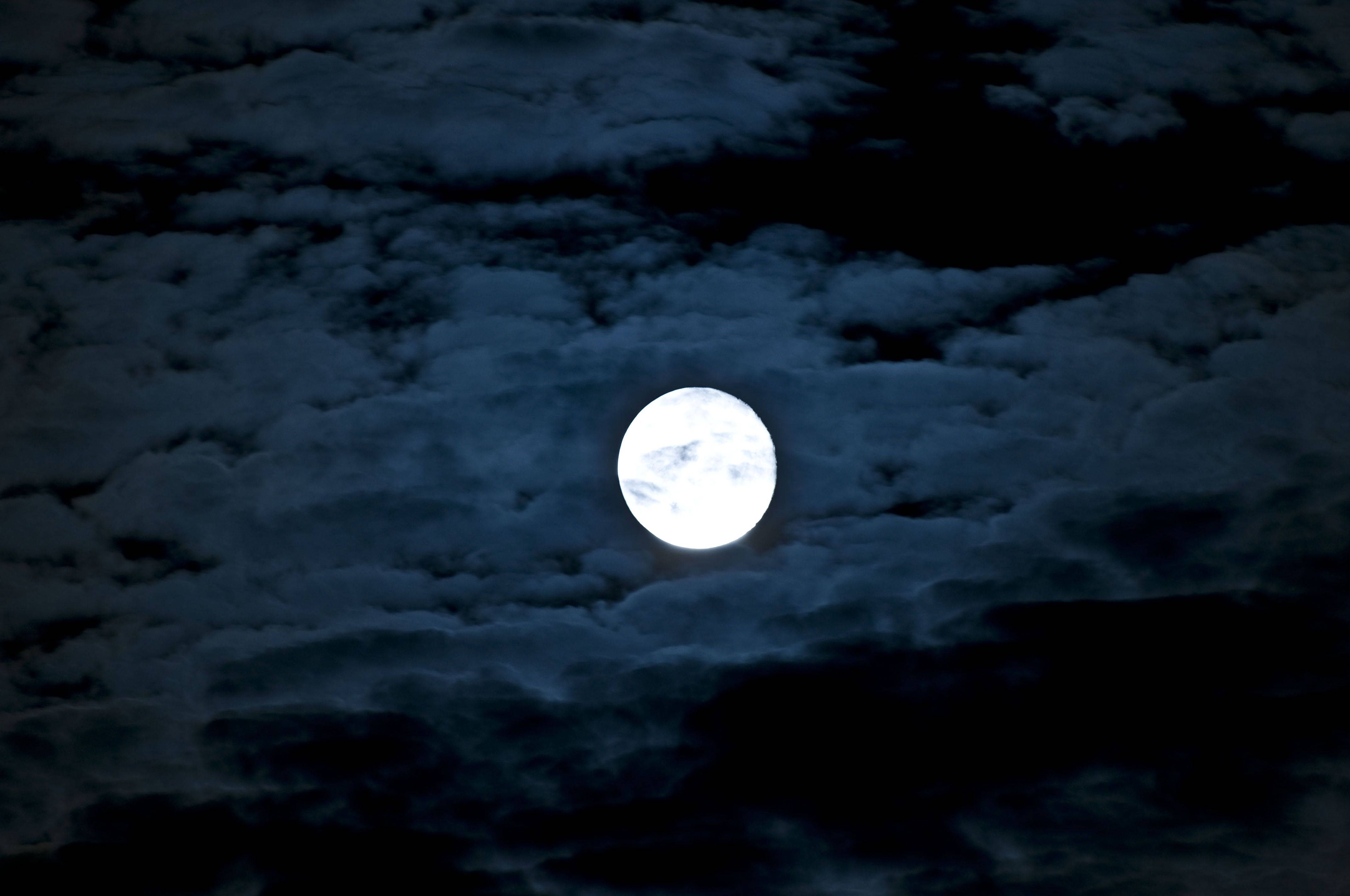 月光 桌布 壁紙 — 一輪明亮的滿月穿透濃密的烏雲，在充滿氛圍的夜空中閃耀。