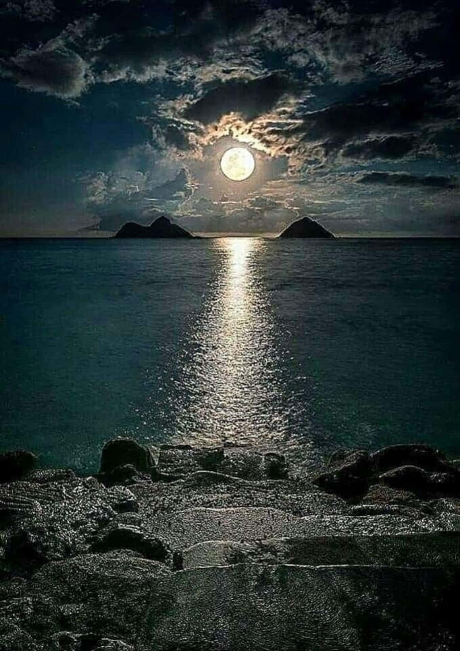 Beautiful Moon 桌布 壁紙 — 一輪明亮的滿月穿透烏雲，映照在平靜的海面上，在兩個遙遠的島嶼之間反射著光芒。