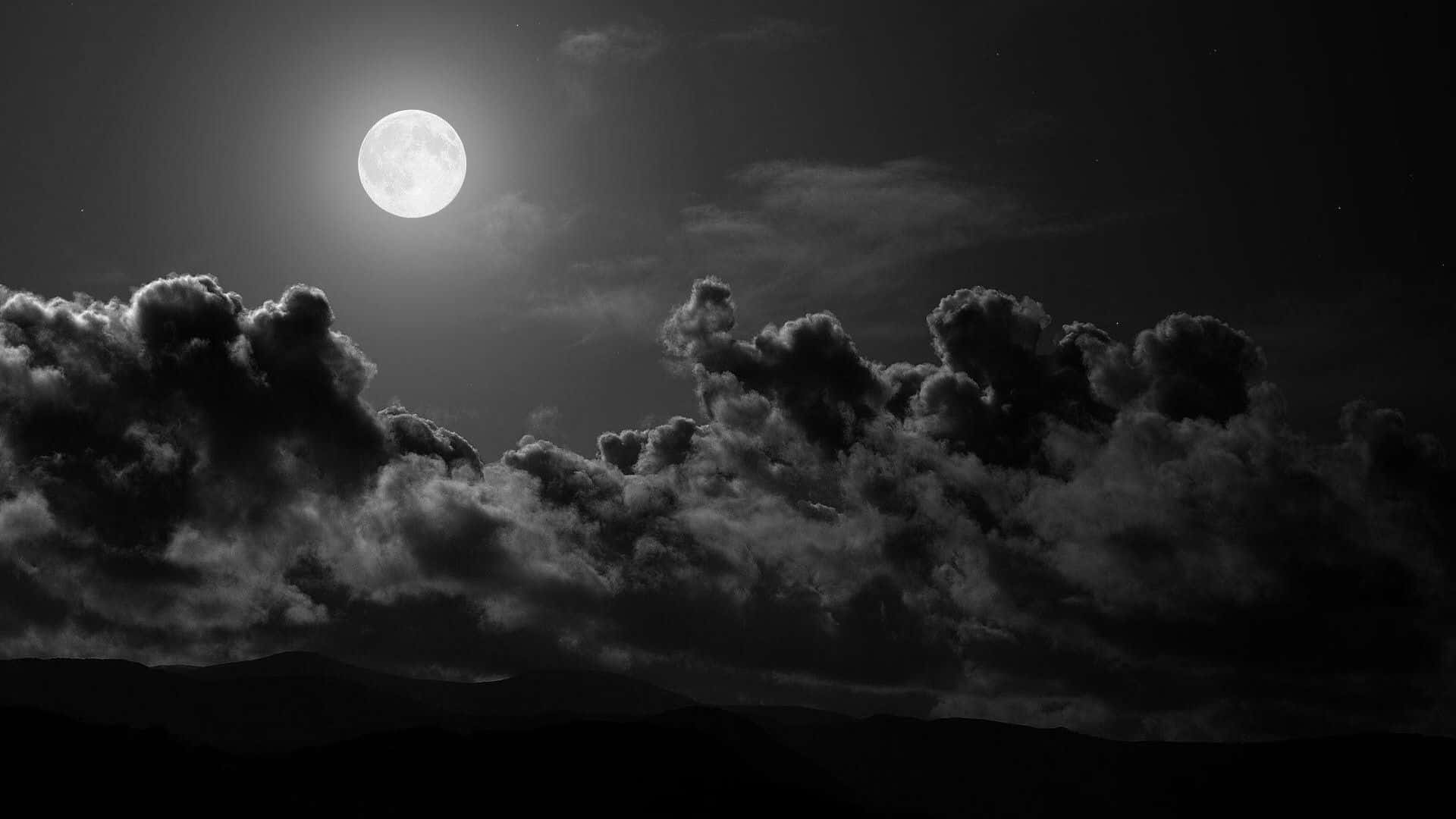 Black And White Aesthetic Pc 桌布 壁紙 — 一輪明亮的滿月穿過戲劇性的雲層，照耀在剪影般的山脈上，呈現出鮮明的黑白夜景。