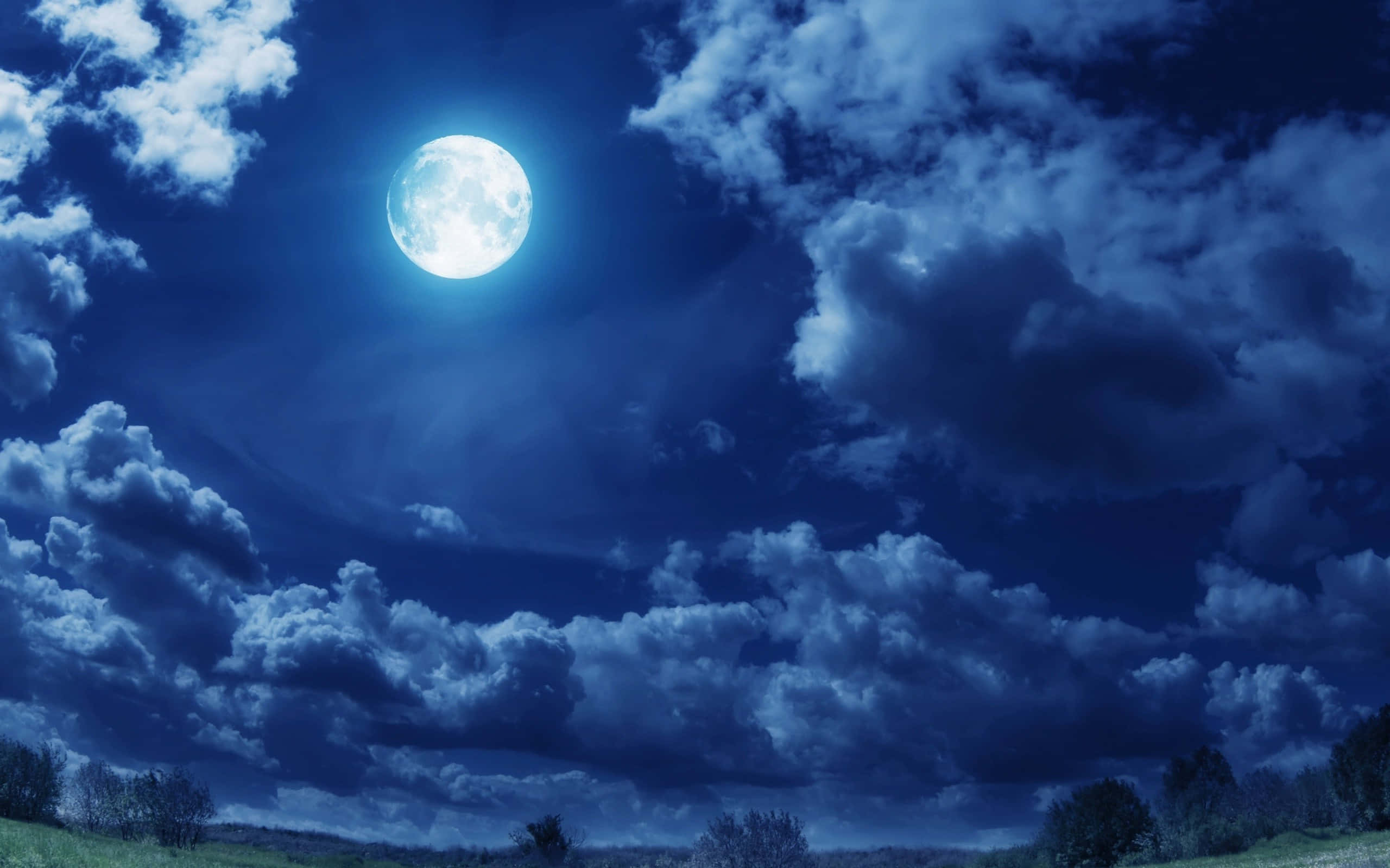 Cool Moon 桌布 壁紙 — 一輪明亮的滿月穿過戲劇性的雲層，照耀在剪影樹木之上的深藍色夜空。