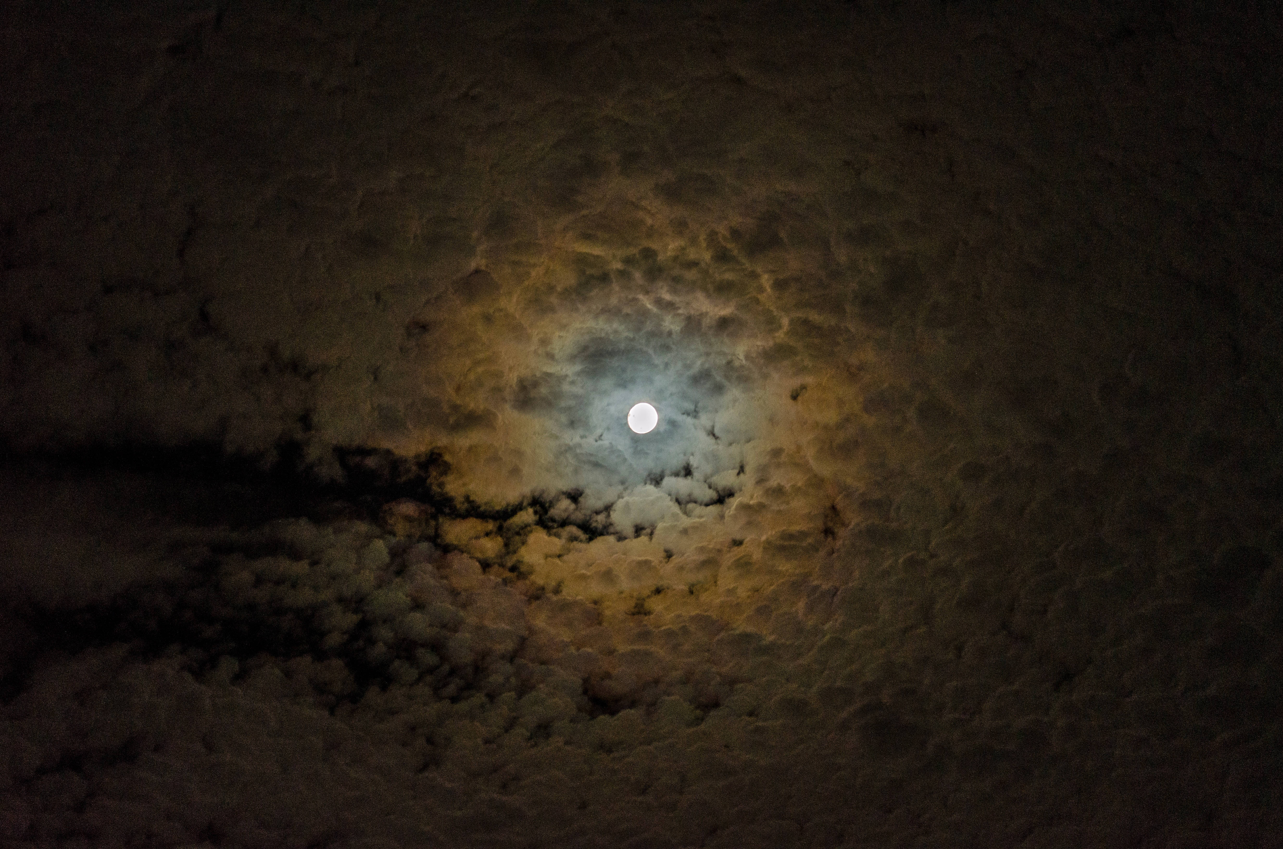 月光 桌布 壁紙 — 一輪明亮的滿月穿過有紋理的雲層，在夜空中投射出溫暖的金色光芒。