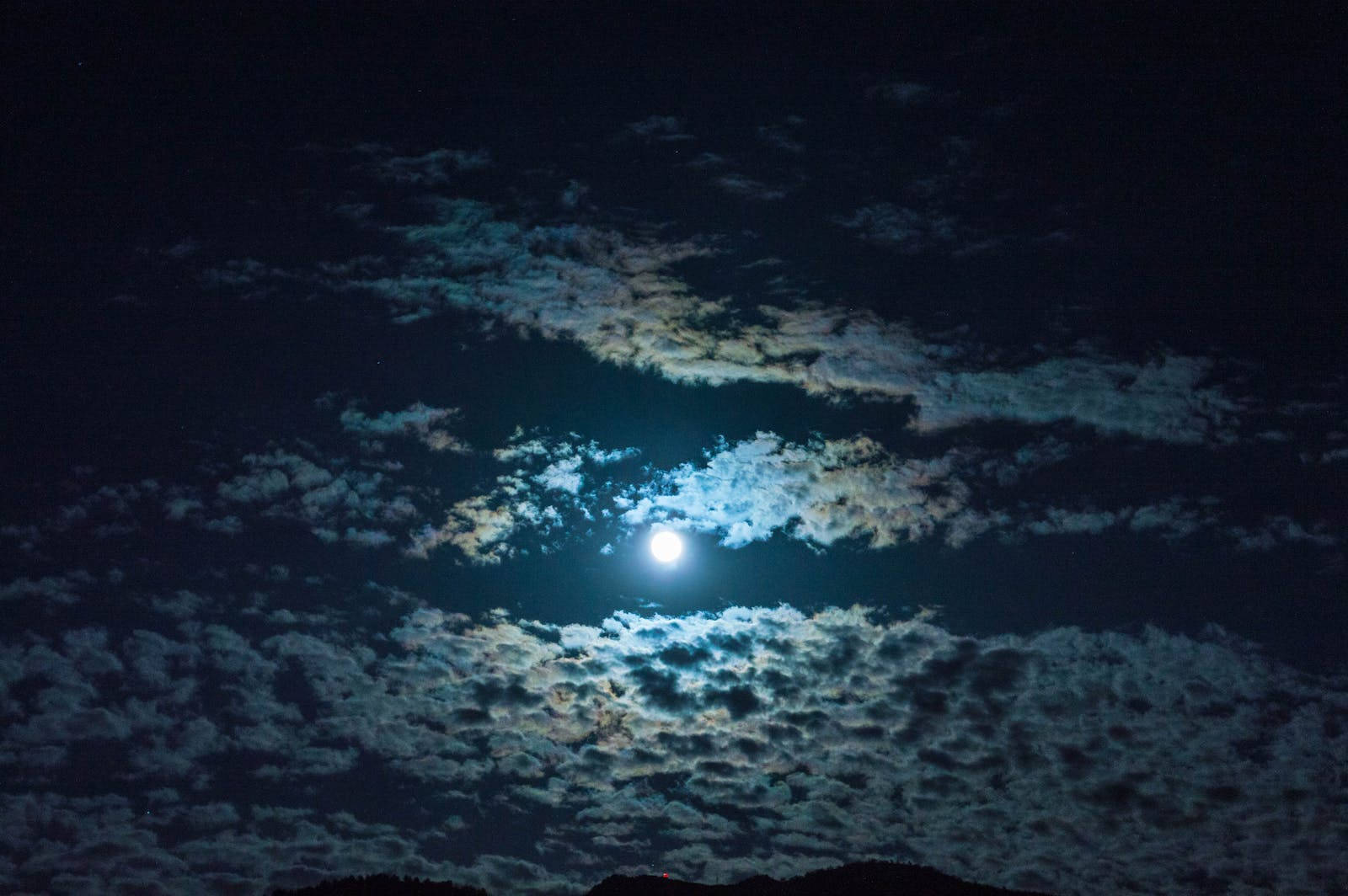 月光 桌布 壁紙 — 一輪明亮的滿月透過縷縷雲層照耀，在黑暗的夜空中投射出空靈的藍色和白色光芒。