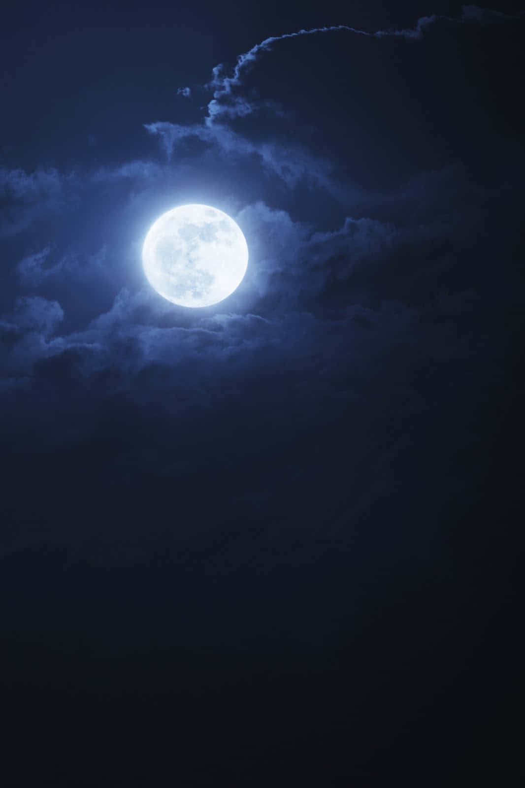 Night Time 桌布 壁紙 — 一輪明亮的滿月透過輕柔的雲層，在深靛藍色的夜空中閃耀。