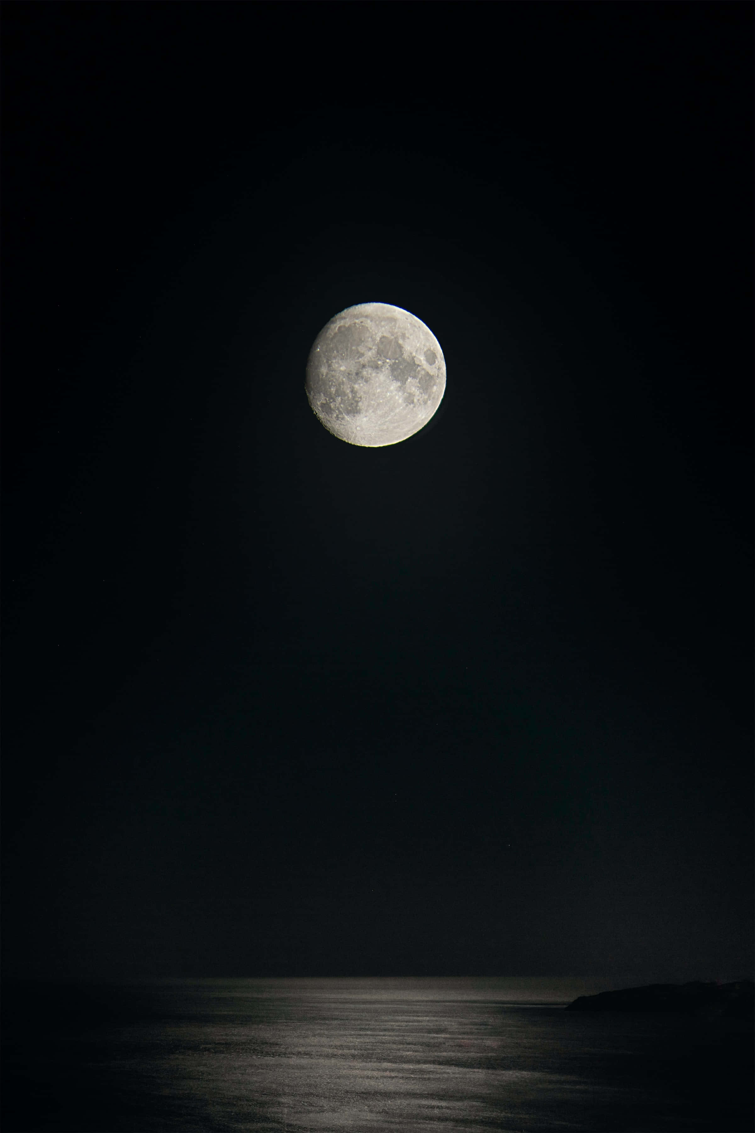 Dark Moon 桌布 壁紙 — 一輪明亮的滿月高懸在平靜的海洋之上，深邃的黑色夜空下。