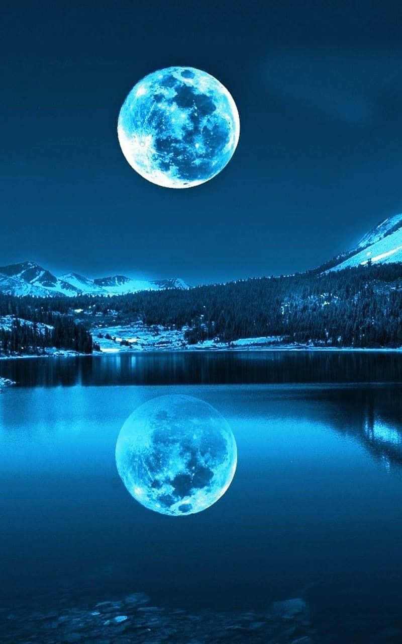 Pretty Moon 桌布 壁紙 — 一輪明亮的藍月懸掛在積雪的山峰上，完美地倒映在寧靜的湖面上，背景是深藍色的夜空。