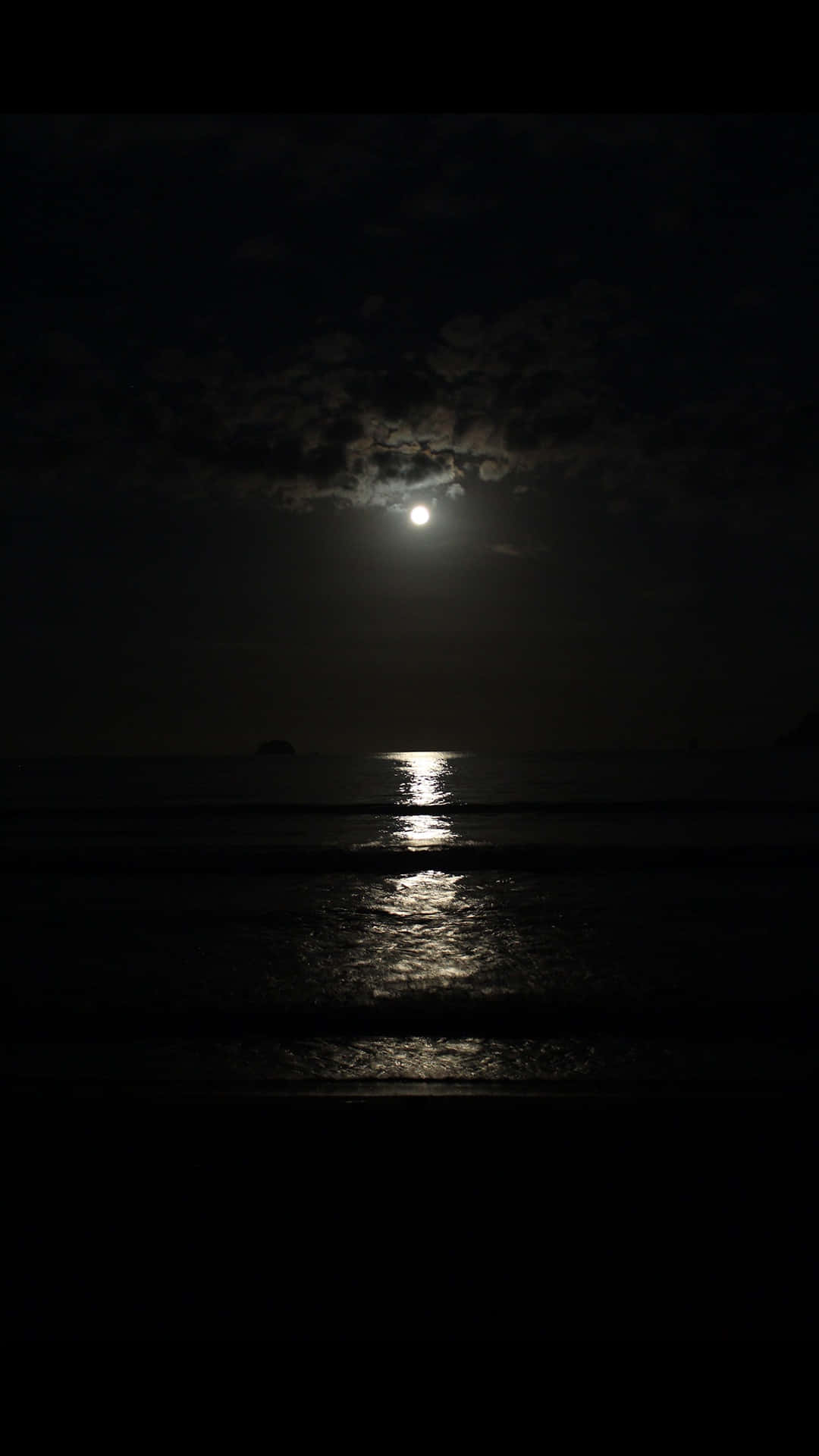 黑夜 桌布 壁紙 — 一輪明月穿過烏雲，在夜晚平靜的海面上投射出一條閃爍的路徑。