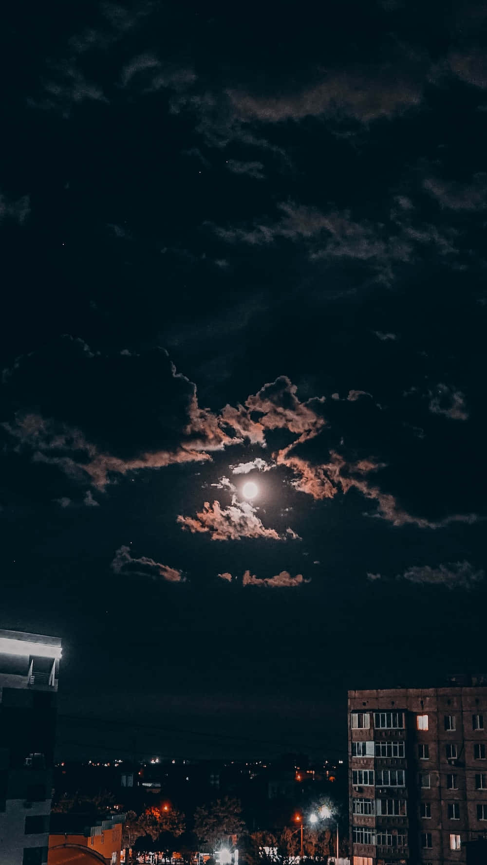 photography iPhone 桌布 壁紙 — 一輪明月透過縷縷雲層照耀在黑暗的城市景觀上，街燈和建築物輪廓閃爍發光。