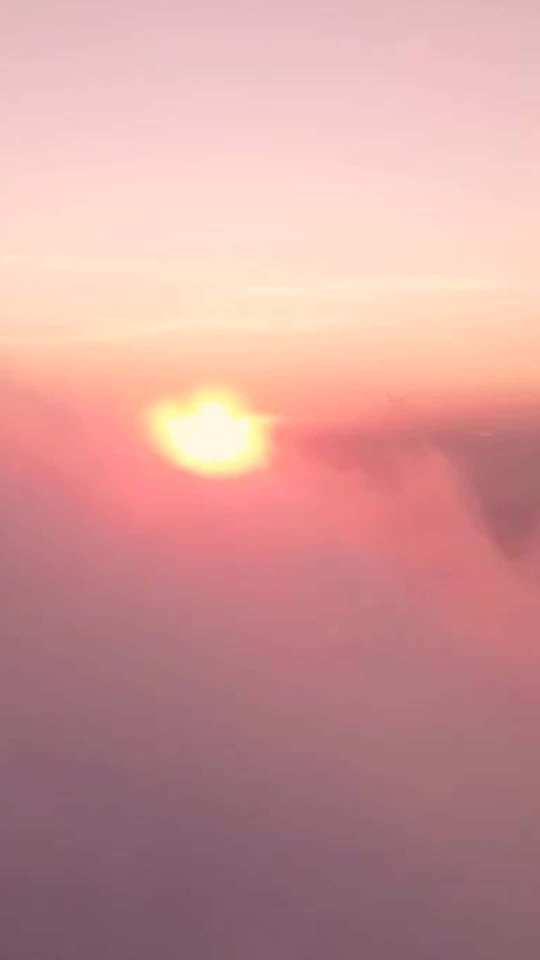 shy sun 壁紙 — 一輪柔和發光的太陽沉入朦朧的地平線下，在天空中投射出溫暖的粉紅色和橙色色調。
