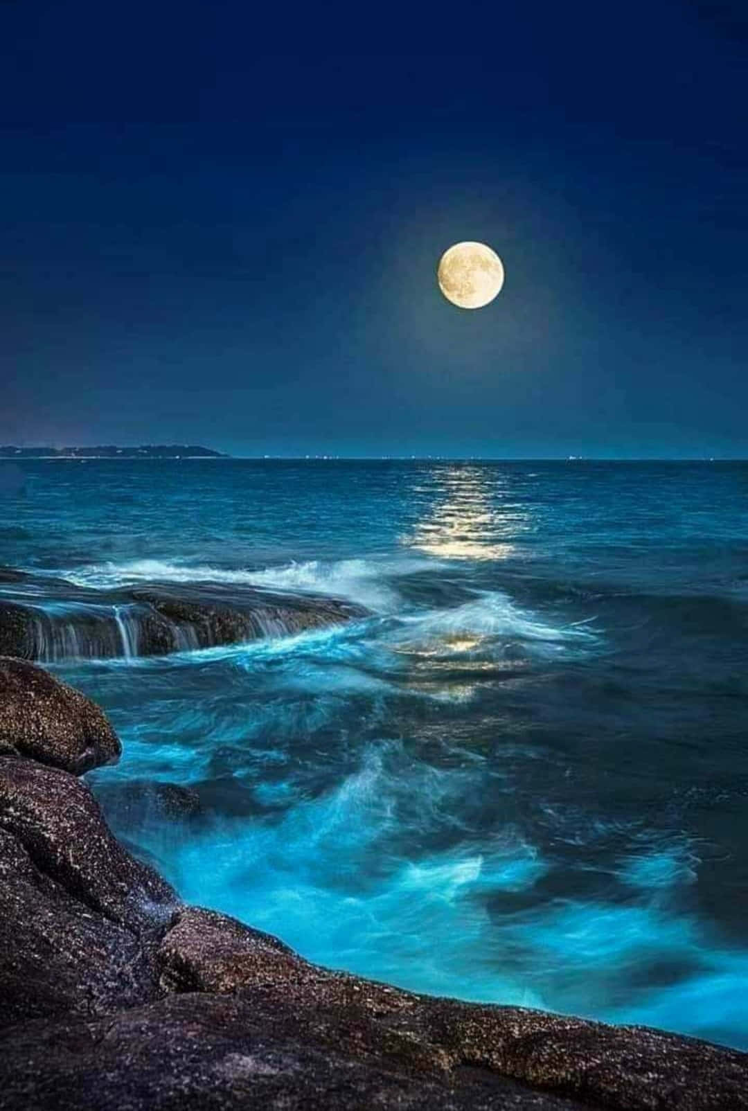 美麗 桌布 壁紙 — 一輪滿月在波濤洶湧的海洋上發光，海浪在深藍色夜空下拍打著黑暗的岩石。