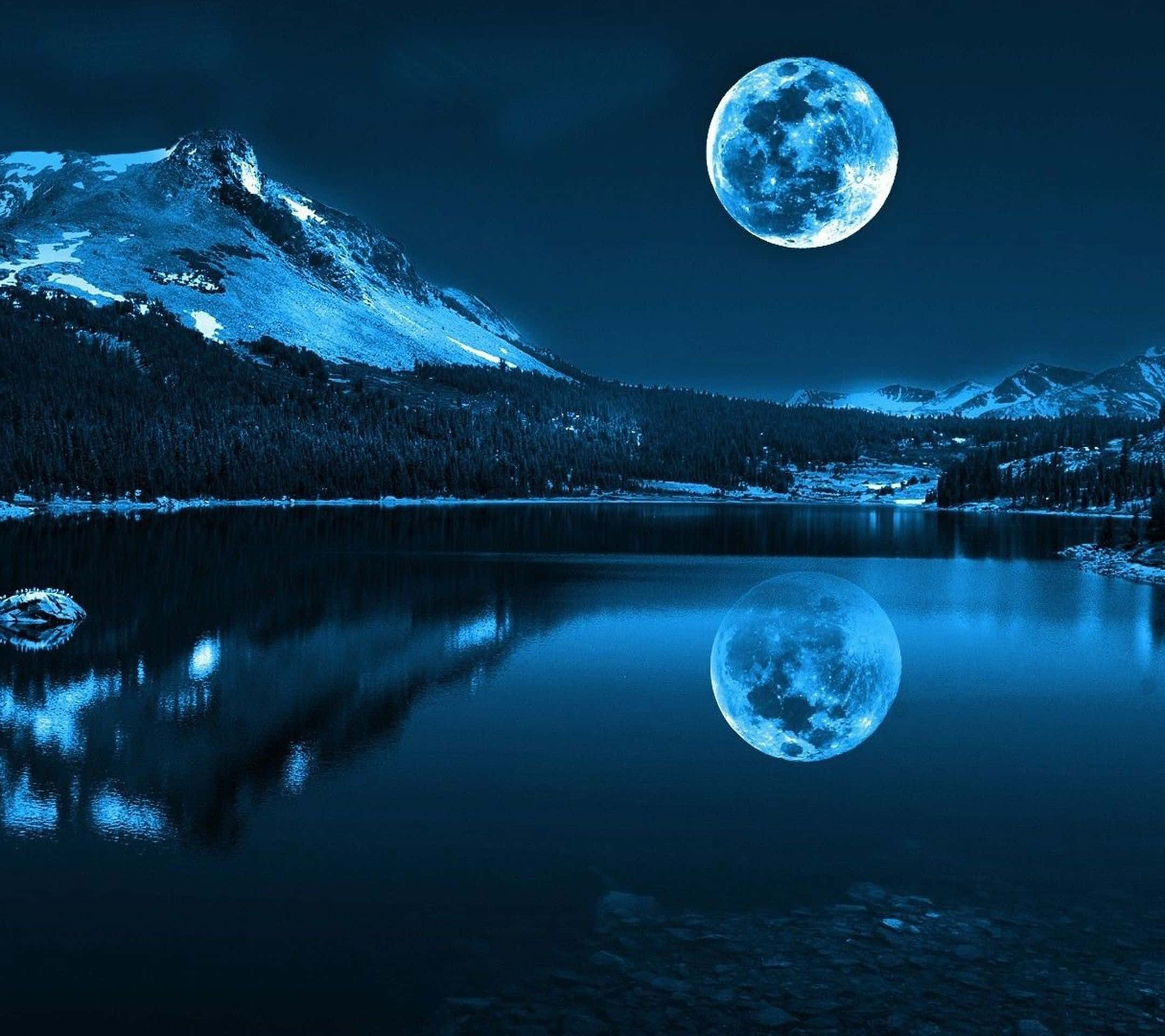 Night Time 桌布 壁紙 — 一輪滿月在積雪的山湖上空發光，將其寧靜的藍光反射在平靜的水面上。